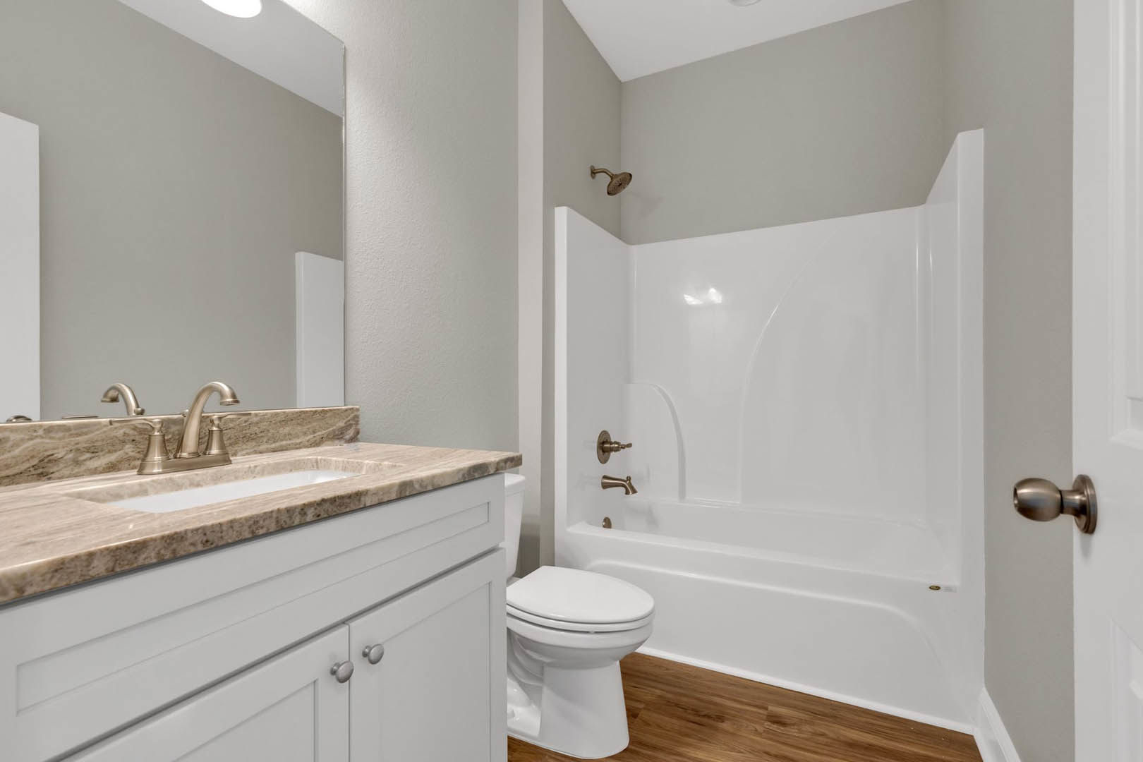 White freestanding bathtub and modern toilet on gray tile floor, light wood vanity with vessel sink, chrome faucet, and neutral wall tiles