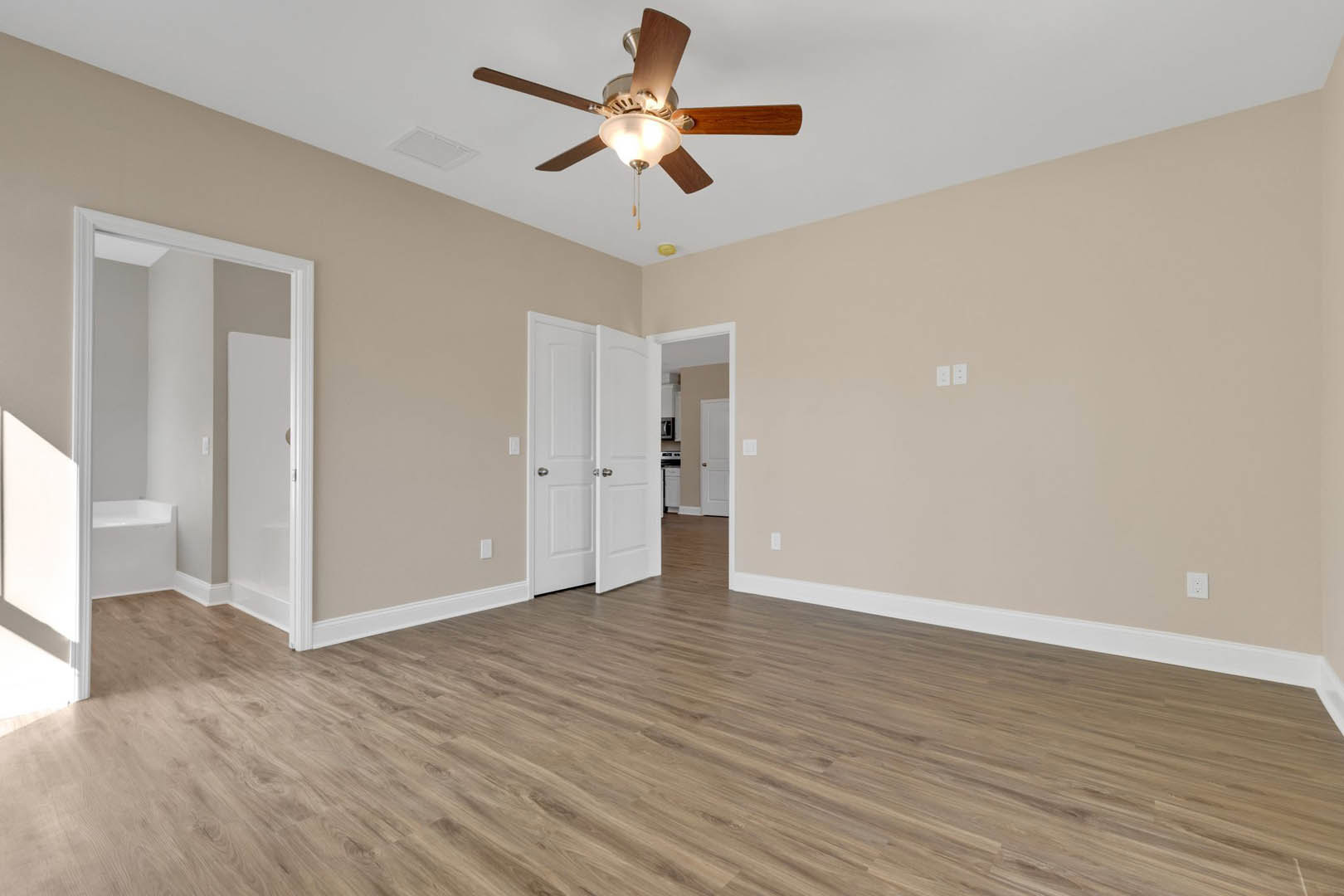 Ceiling fan with light fixture above wood flooring, white walls, white door with silver knobs, and decorative molding