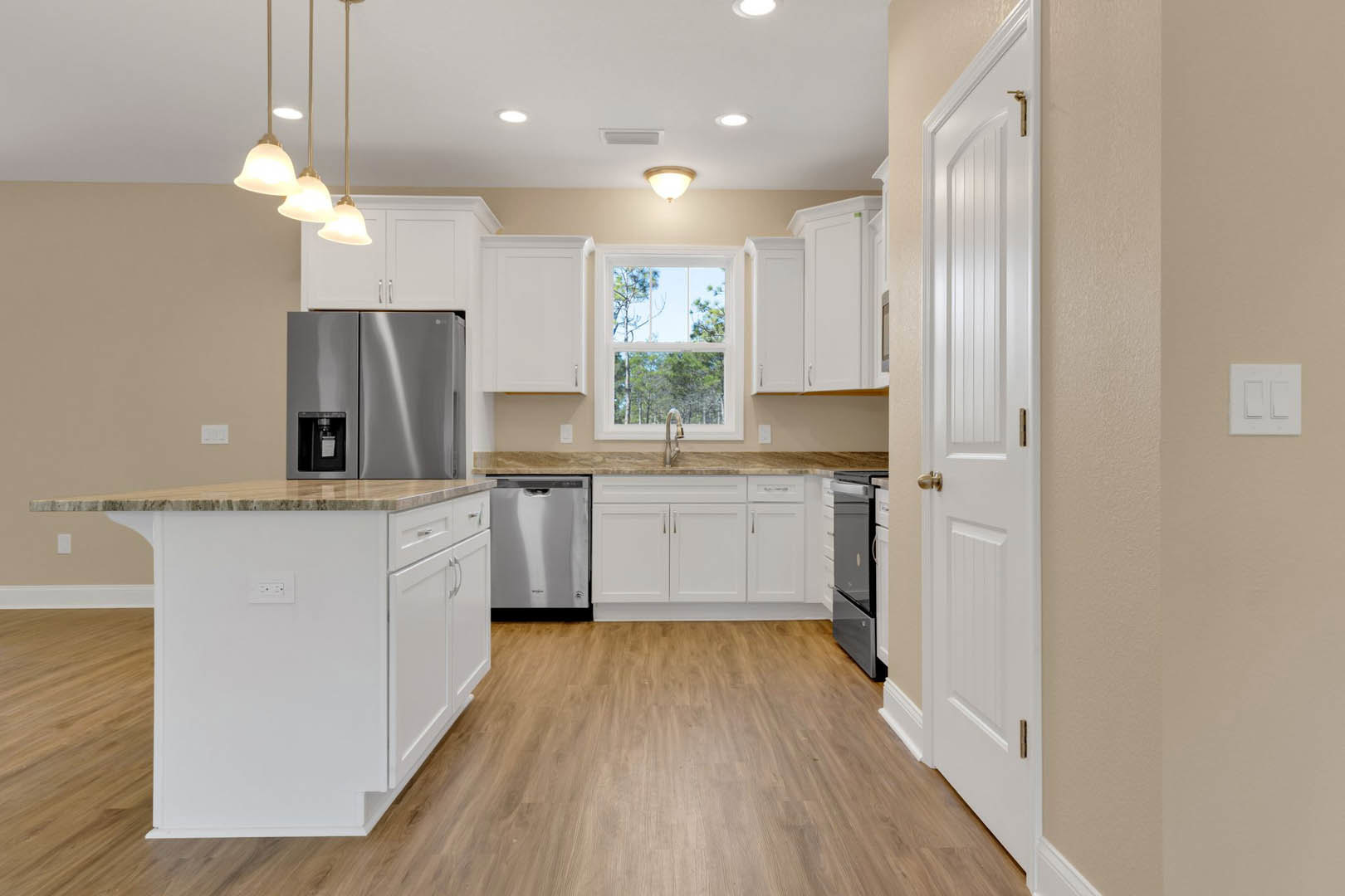 White kitchen cabinets with brushed metal hardware, wood plank flooring, stainless steel refrigerator, quartz countertops, and a person standing by a large window.