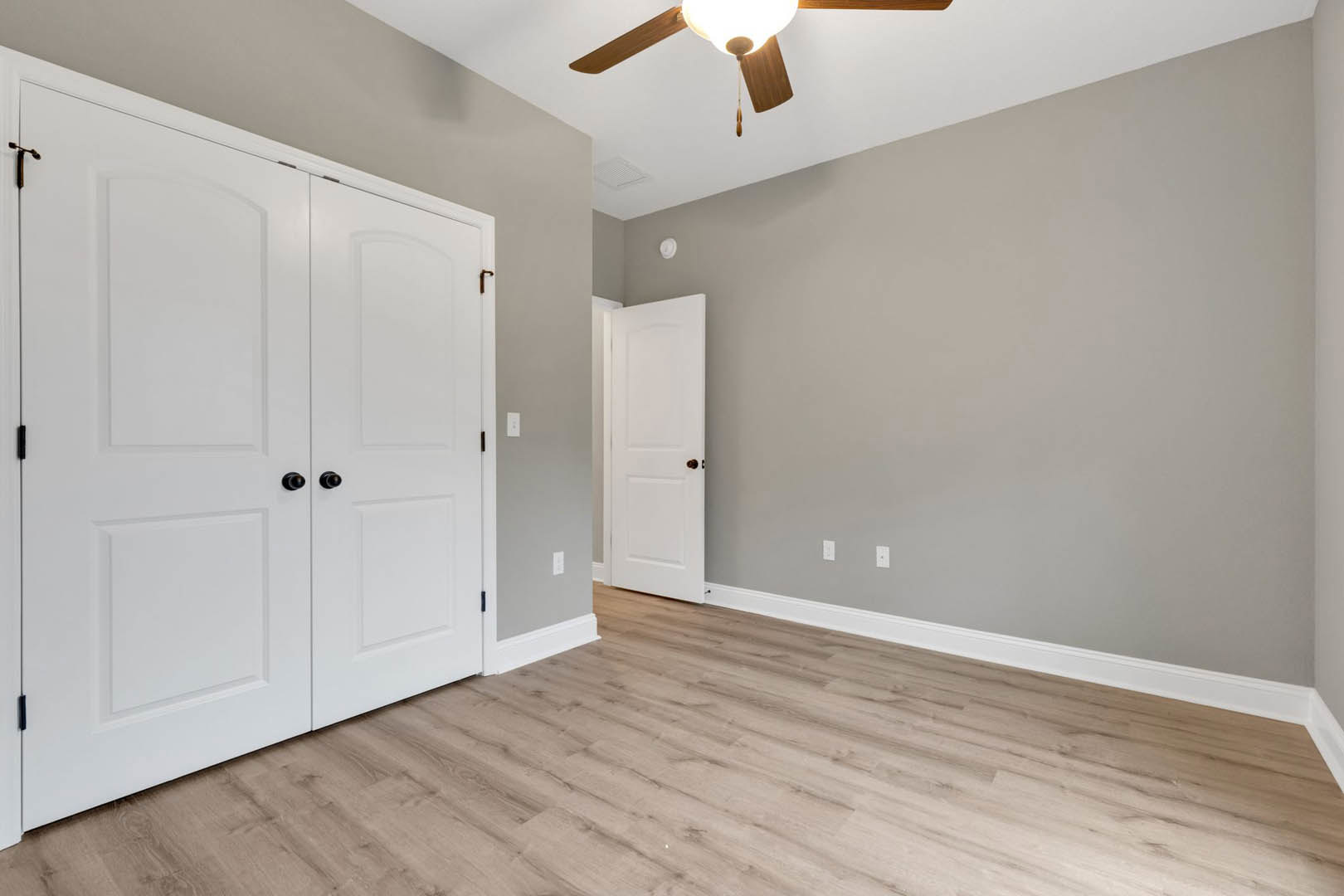 Room with wood flooring, white trim, white doors featuring gold and black hardware, and a ceiling fan mounted on a white ceiling.