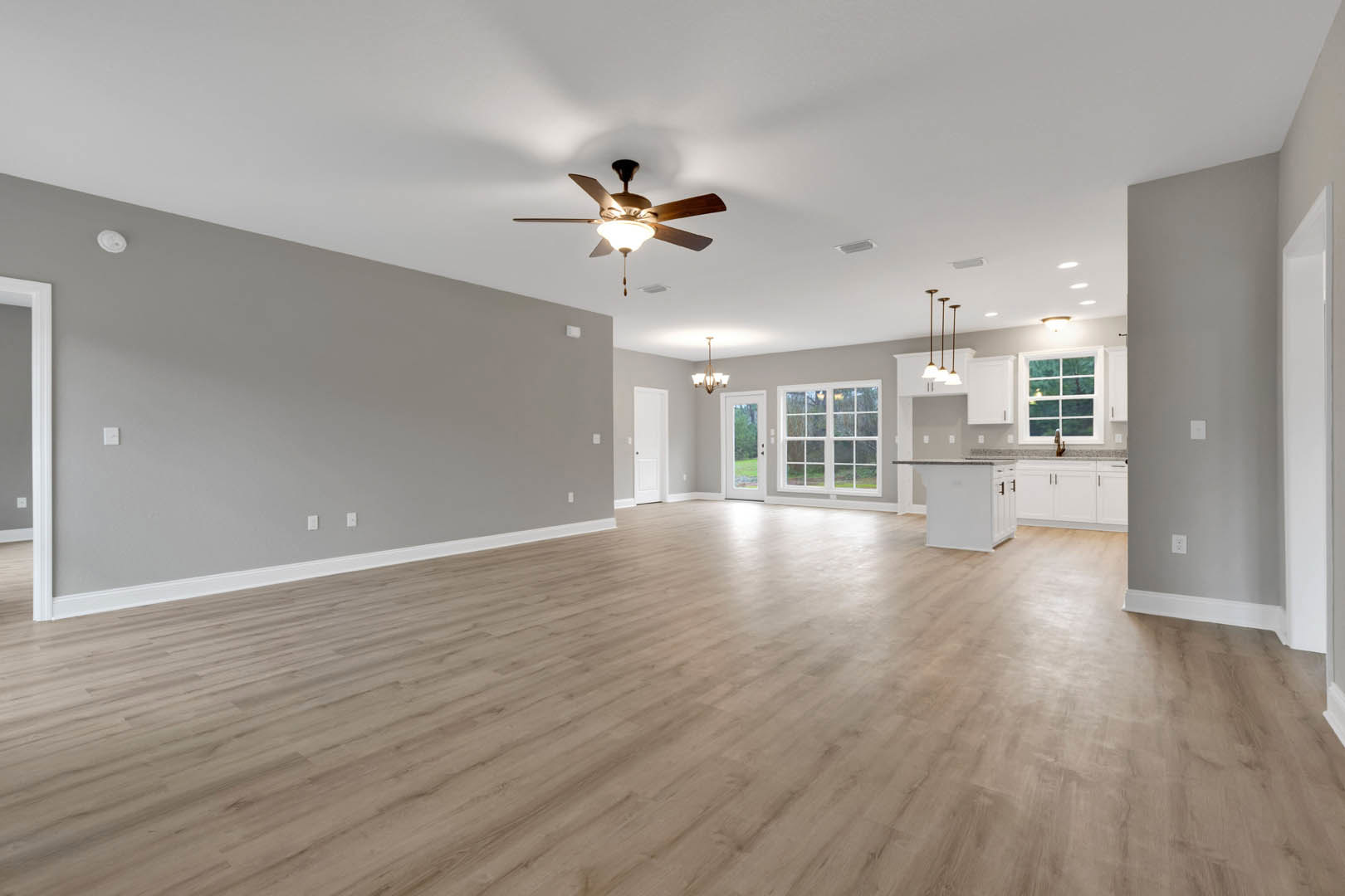 Spacious room featuring hardwood flooring, white plaster walls, multi-pane window overlooking trees, and a ceiling fan with integrated light fixture