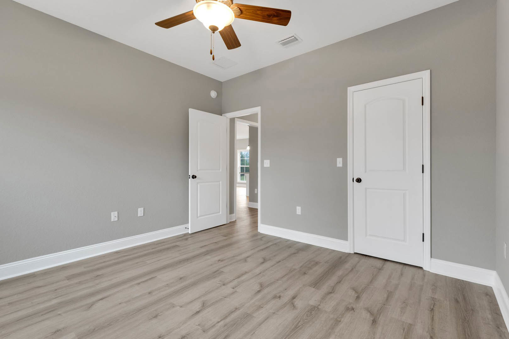 Room with wood flooring, white baseboards, white doors featuring black handles, and a ceiling fan with integrated light fixture.