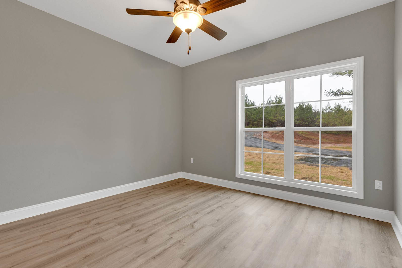 Ceiling fan with light fixture mounted on white ceiling, large window with view of trees, wood flooring, and white wall with crown molding