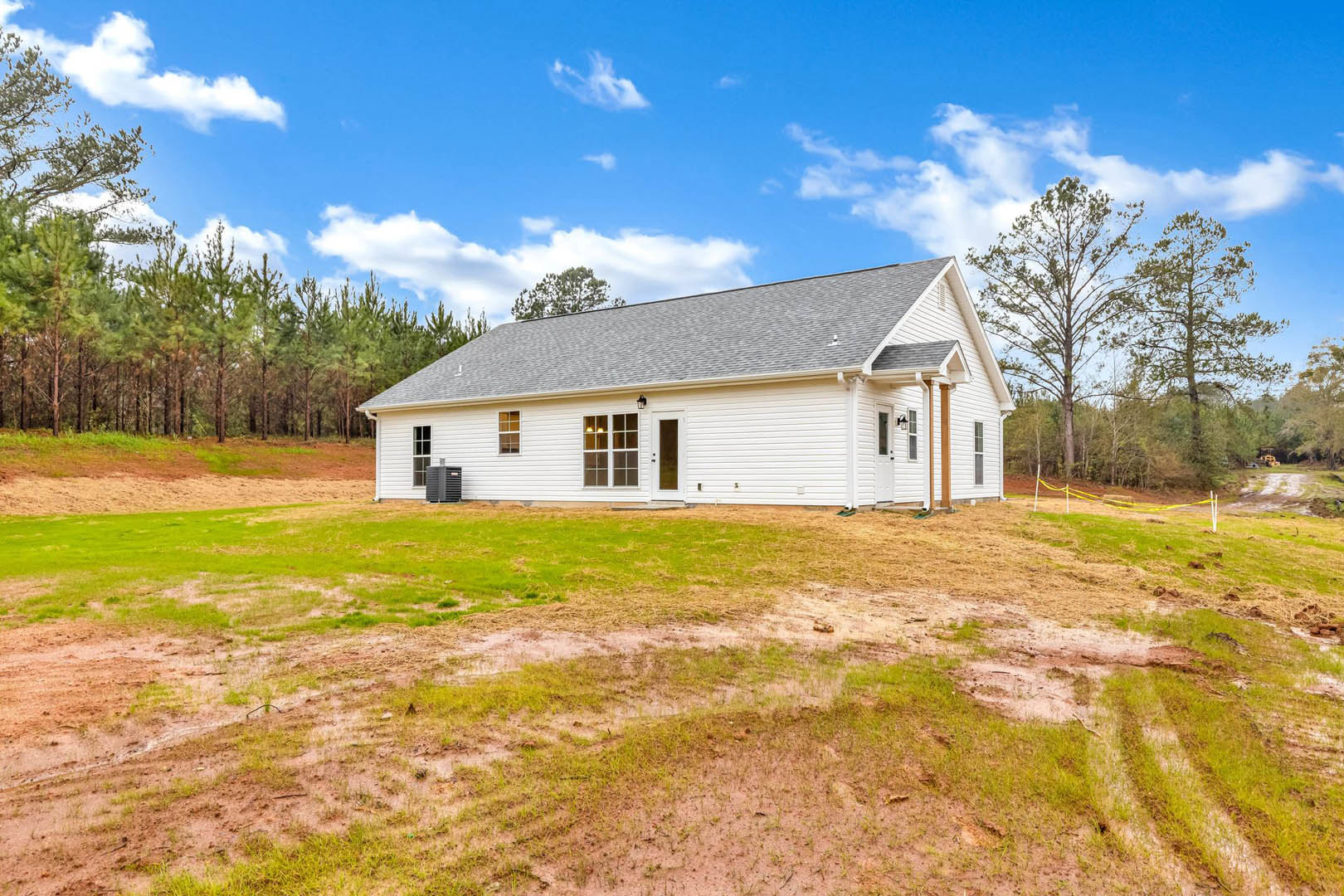 White farmhouse with pitched roof, illuminated rooftop light, surrounded by green lawn and leafless tree under blue sky with scattered clouds