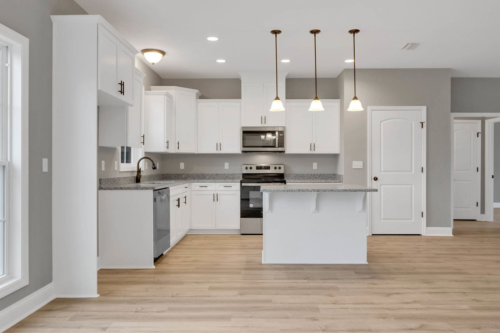 White kitchen cabinets, marble countertop, stainless steel appliances, wood flooring, undermount sink, and tile backsplash