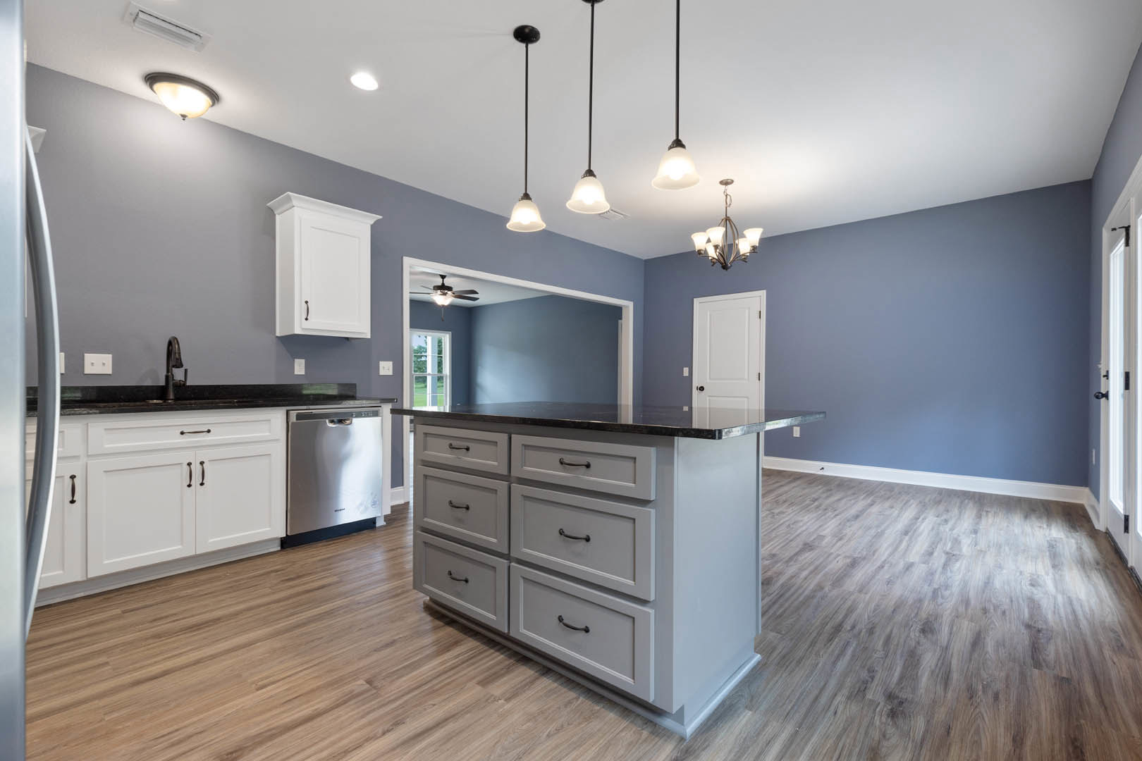 Kitchen with wood flooring, central island featuring white cabinetry and silver dishwasher, overhead pendant lights, close-up of drawers and light fixture with exposed bulb