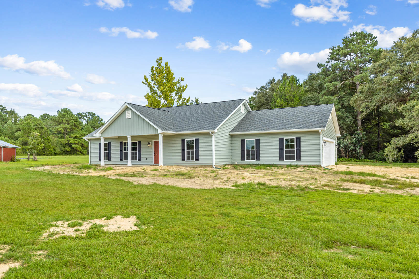 Red farmhouse with metal roof, white trim windows, green lawn, and mature trees in the background