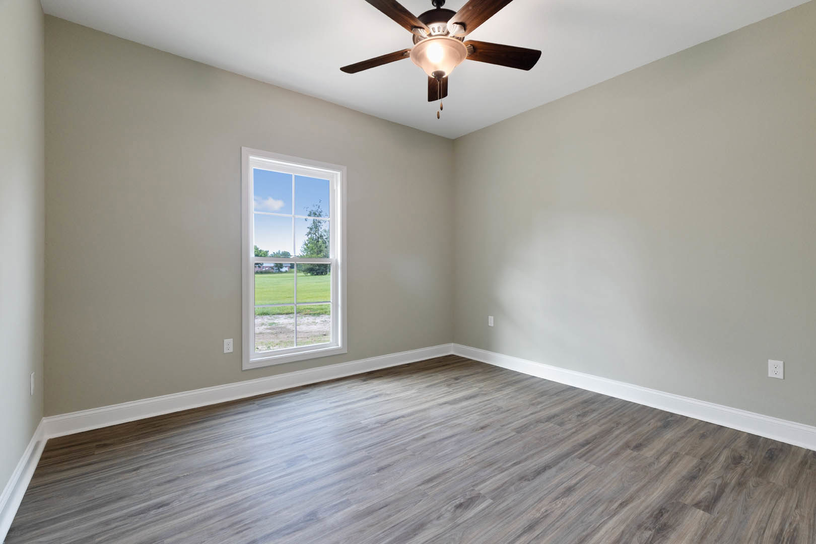 Wood flooring in a bright room featuring a large window overlooking a green lawn, white walls with crown molding, and a ceiling fan with integrated light fixture.