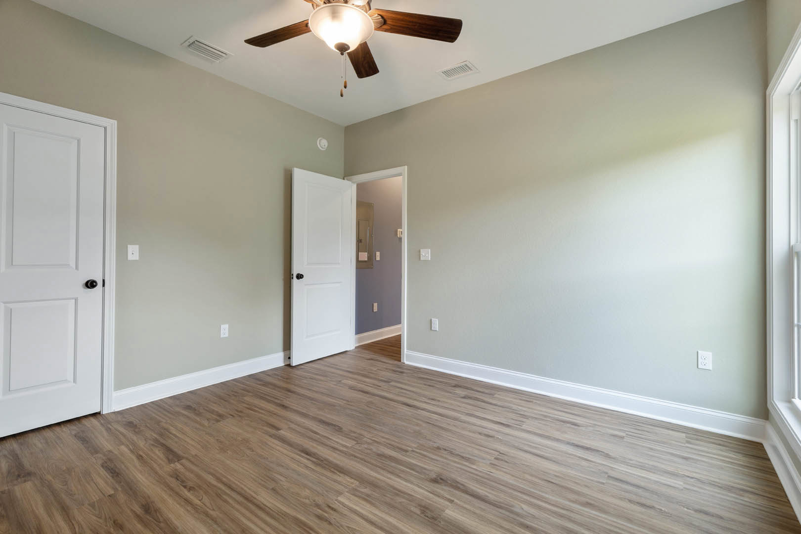 White paneled door with black hardware, wood laminate flooring, ceiling fan with light fixture, white walls, and light switch.