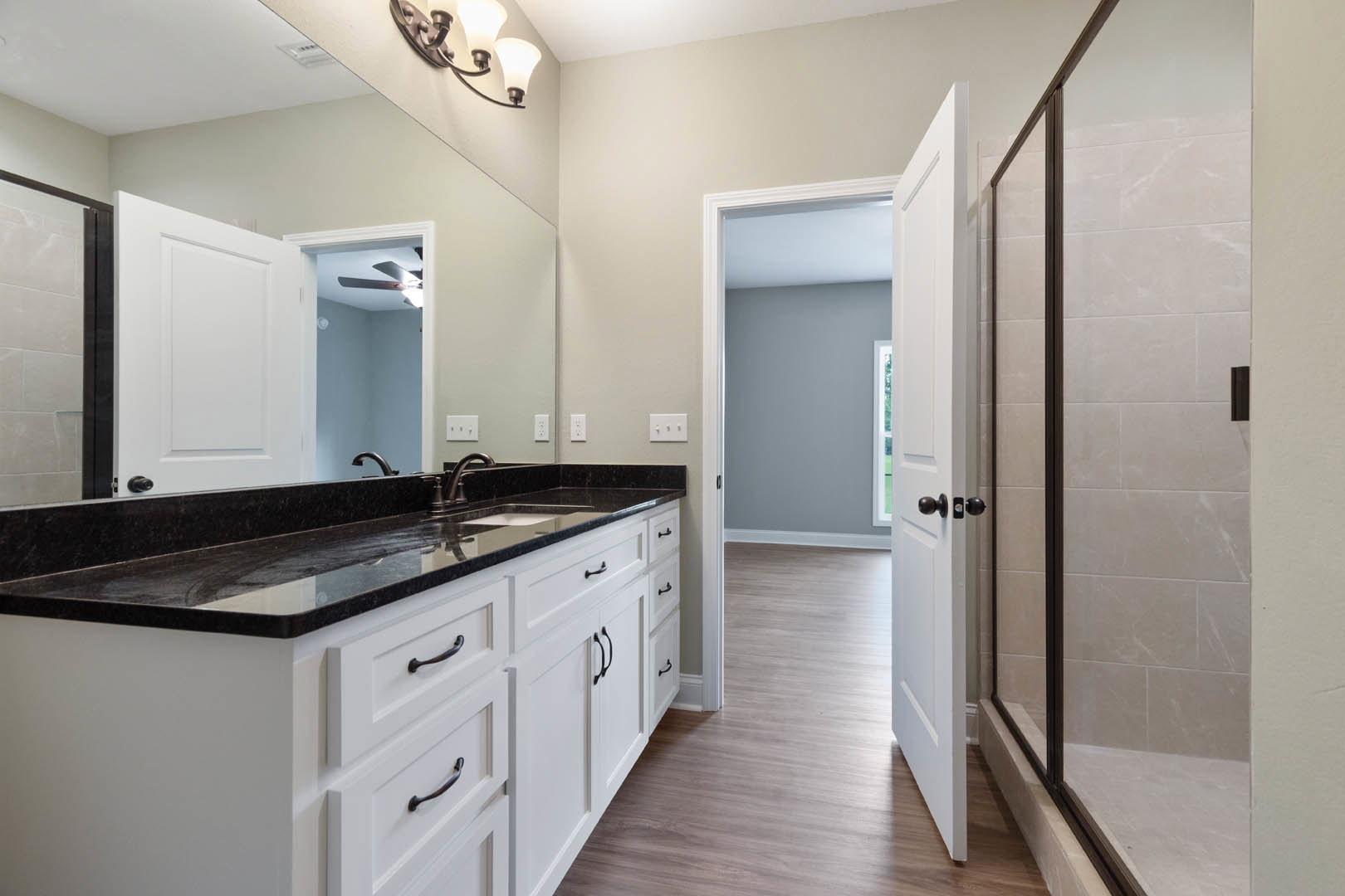 White bathroom featuring a wide mirror above a sleek black countertop with integrated sink, white cabinetry, and modern light fixture.