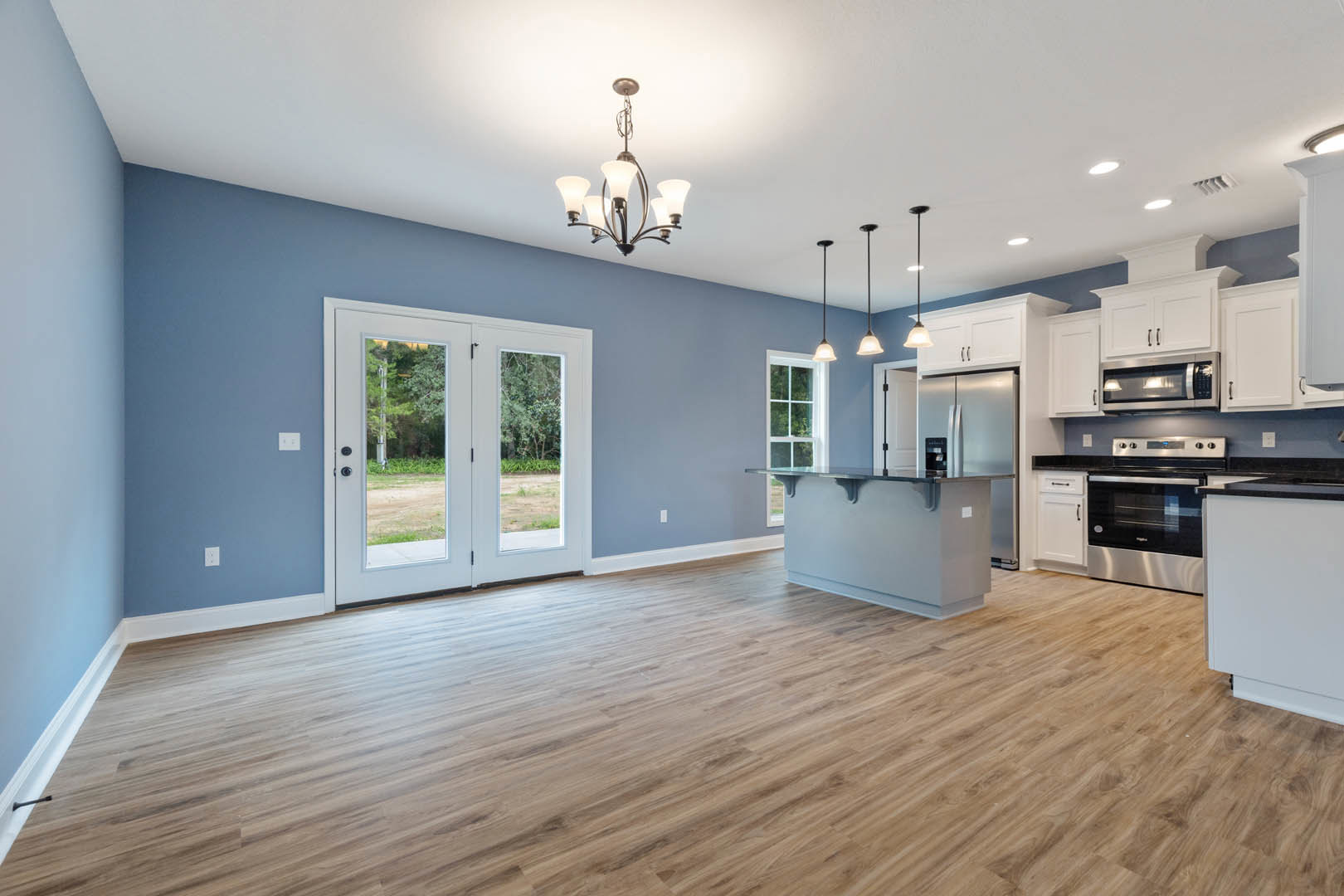 Open kitchen and dining area featuring hardwood flooring, white cabinetry, glass-paneled double doors, stainless steel stove, large window, and modern chandelier.