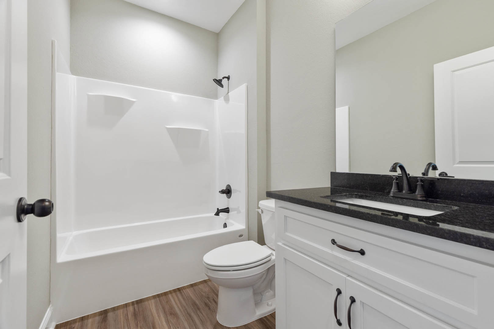 White bathtub and toilet against light tile walls, chrome faucet, white cabinetry, and brushed metal door handle visible in foreground