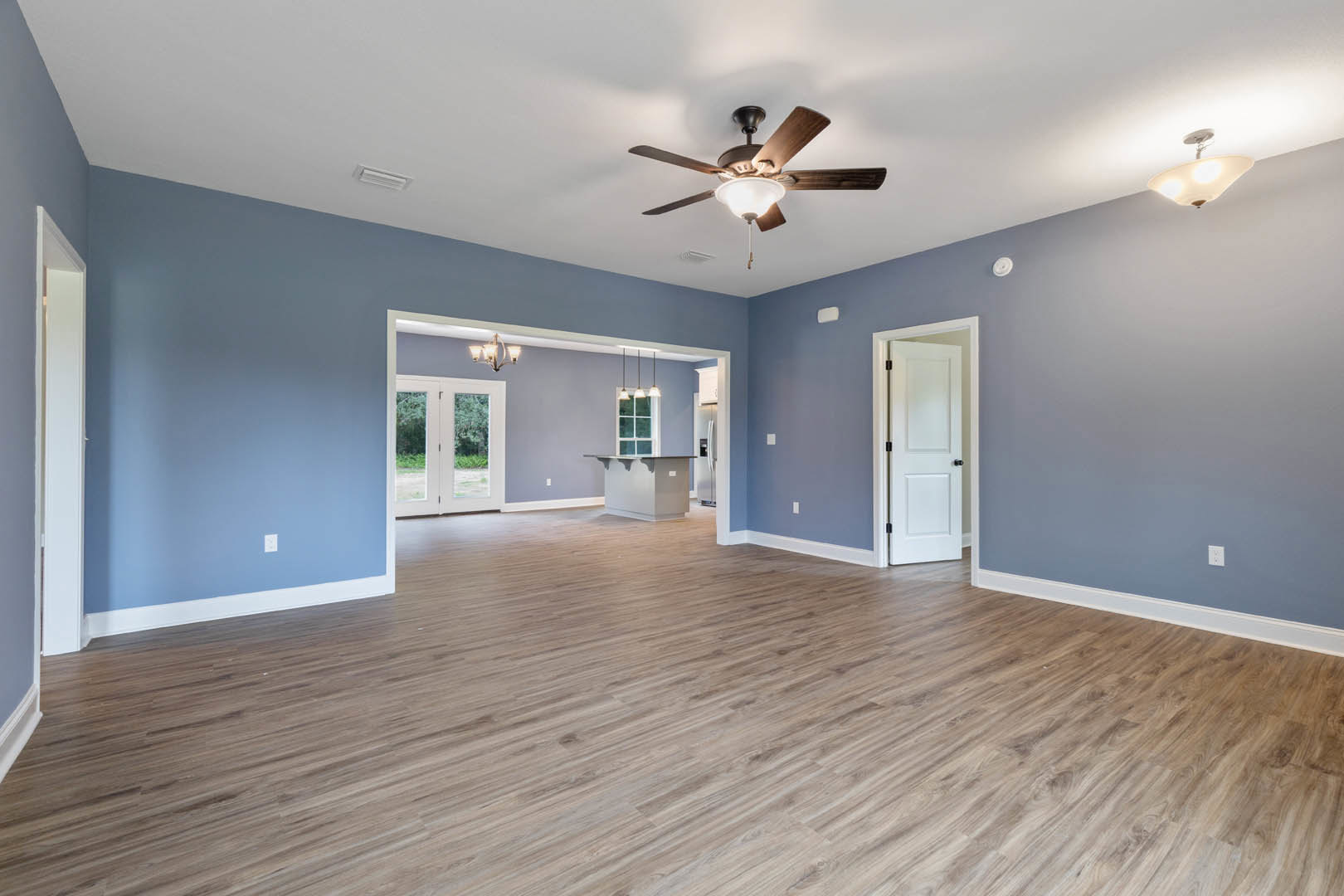 Blue walls and wood flooring in a room with a ceiling fan and light fixture, white door with black knobs, double glass-paneled doors, and white shade light fixture