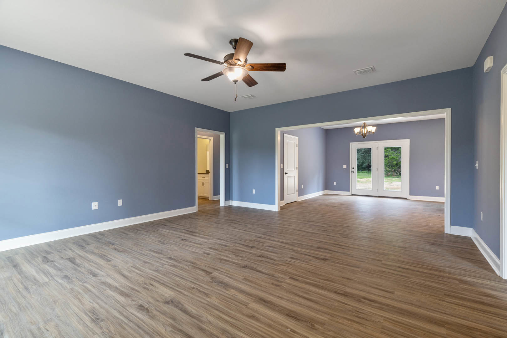 Ceiling fan with light fixture, wood flooring, blue walls, white double door with glass panes, adjacent white door with black knob