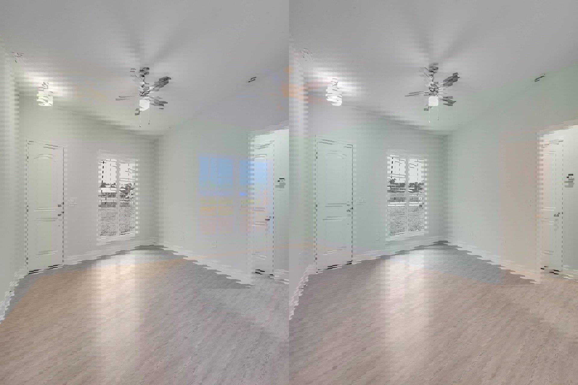 Room with wood flooring, white plaster walls, white door with silver handle, ceiling fan with light, window overlooking grassy field