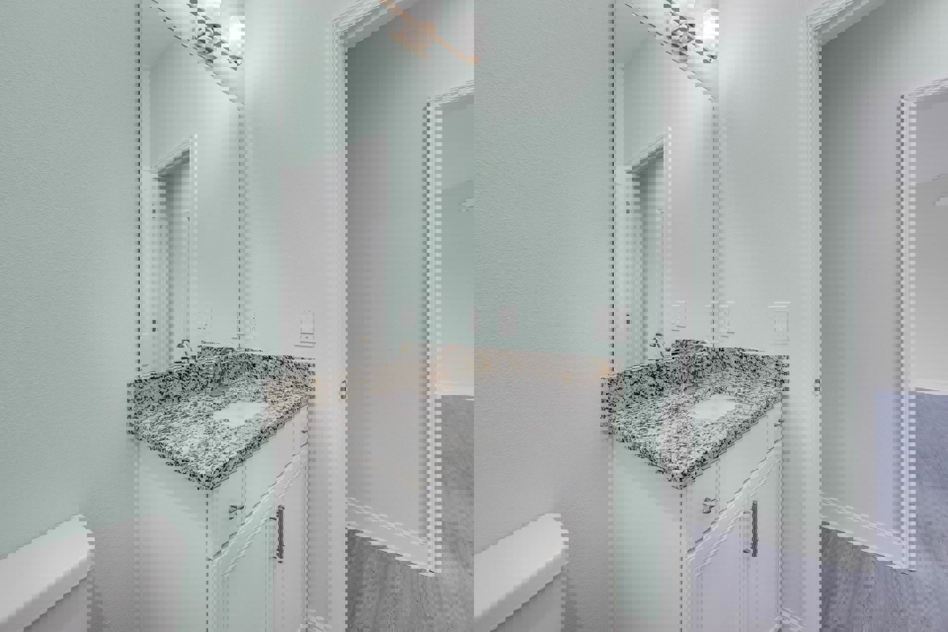 Marble countertop with undermount sink, chrome faucet, white cabinetry, close-up of toilet seat, tiled walls, dual light switches, recessed ceiling light