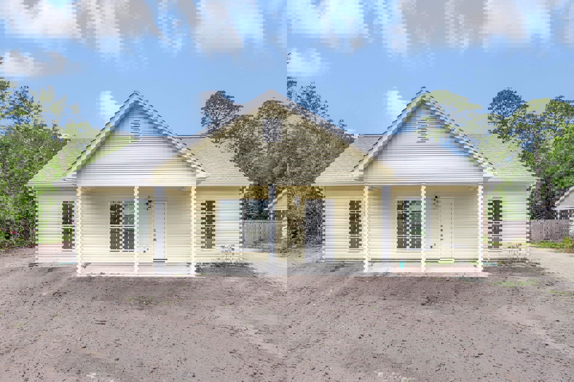 Yellow house exterior with white door, white-framed window, wall vent, and dirt yard under cloudy sky