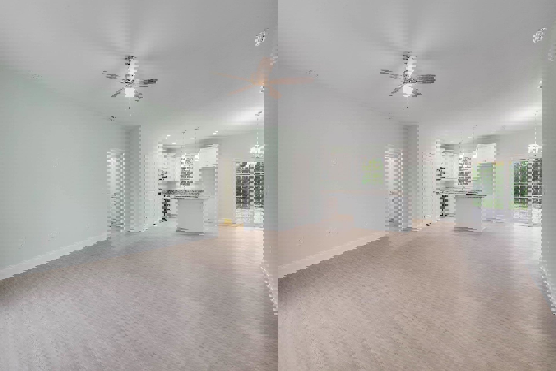 Open living area with white walls, laminate wood flooring, ceiling fan with light, visible kitchen featuring white cabinetry, stainless steel appliances, and a white sliding glass