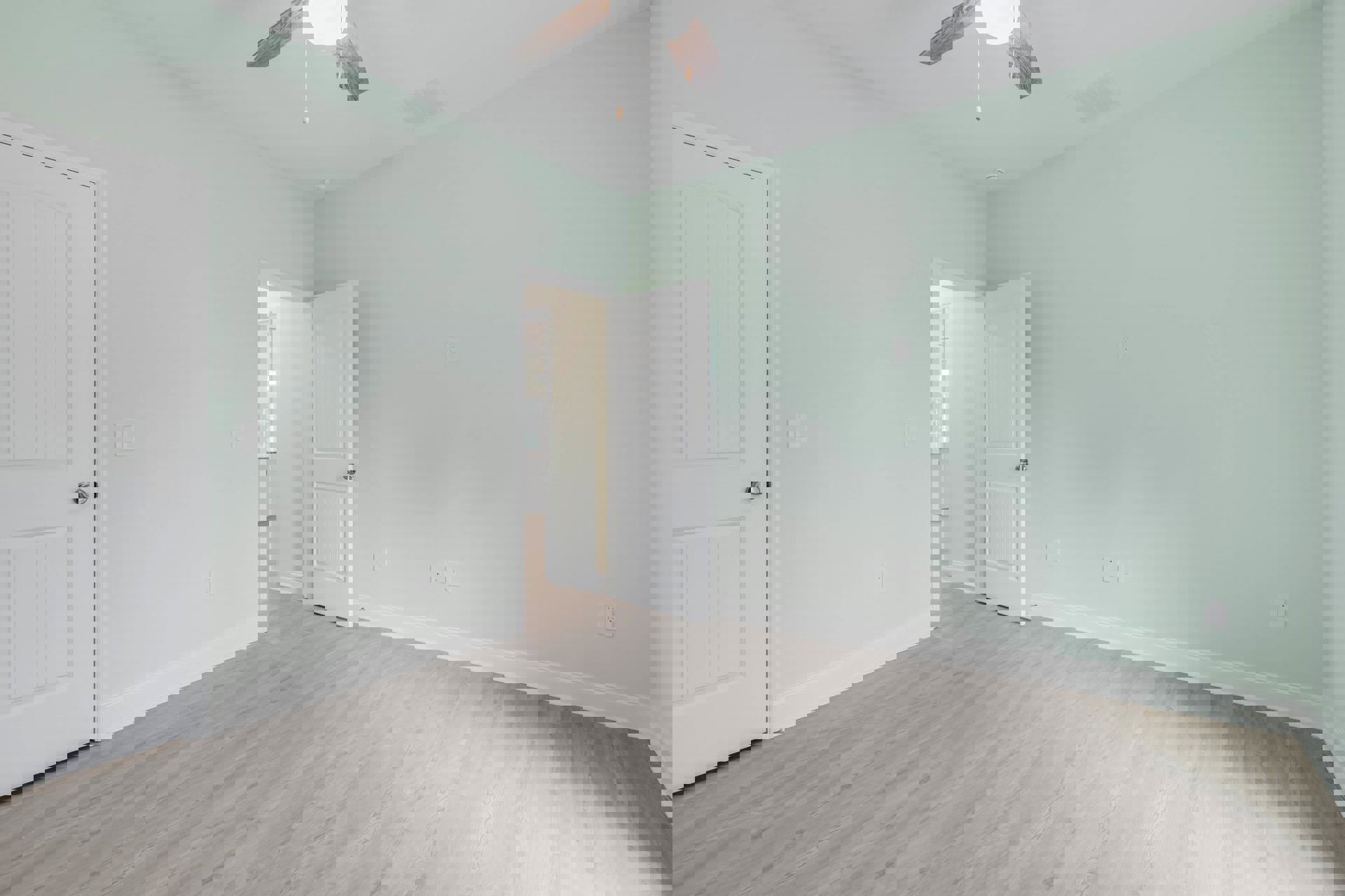 White paneled door with silver knob, white wood laminate flooring, ceiling fan with light fixture, pale walls, crown molding