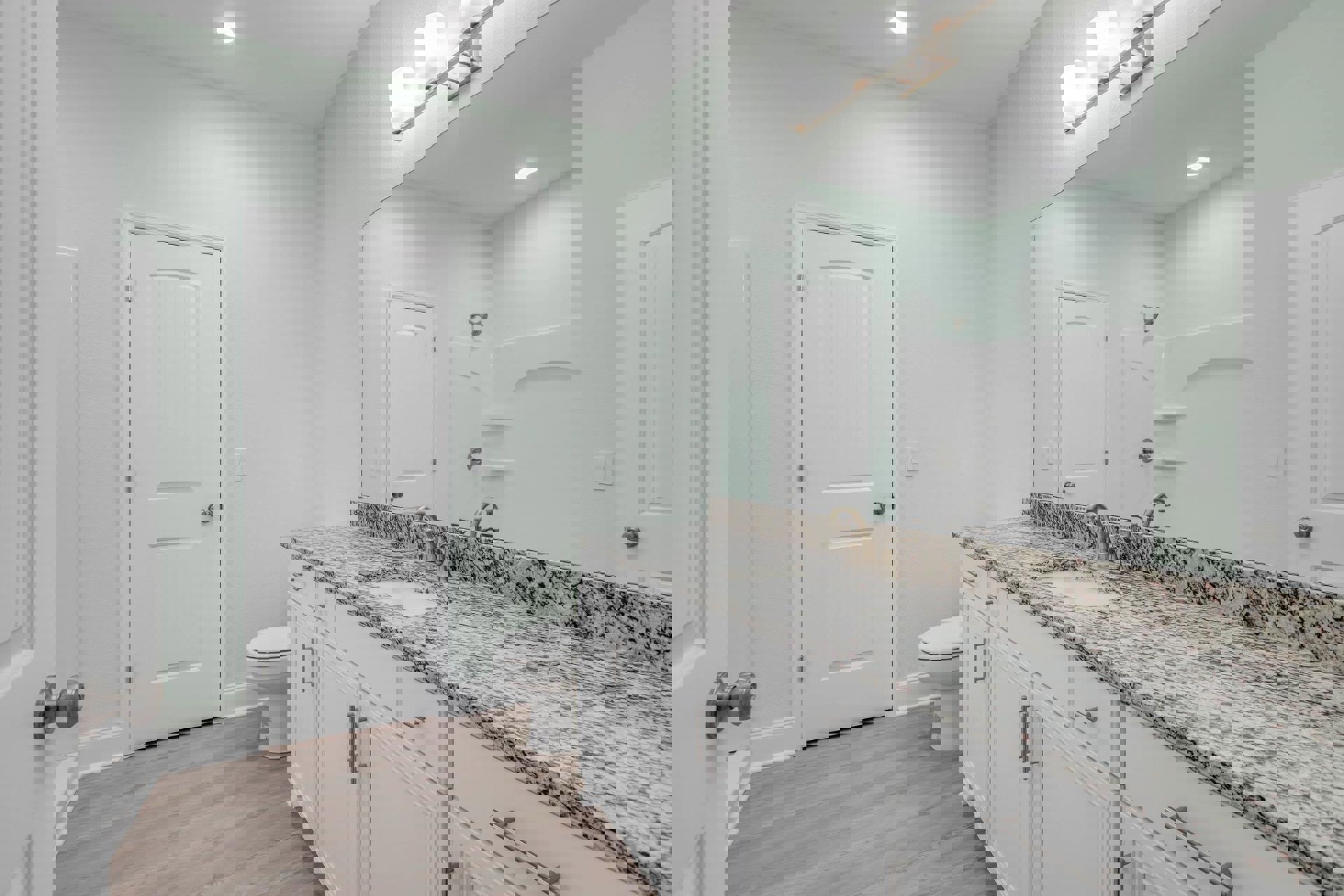 Bathroom with marble countertop, undermount sink, silver faucet, white toilet, wood flooring, white door with silver handle, white walls, recessed ceiling light