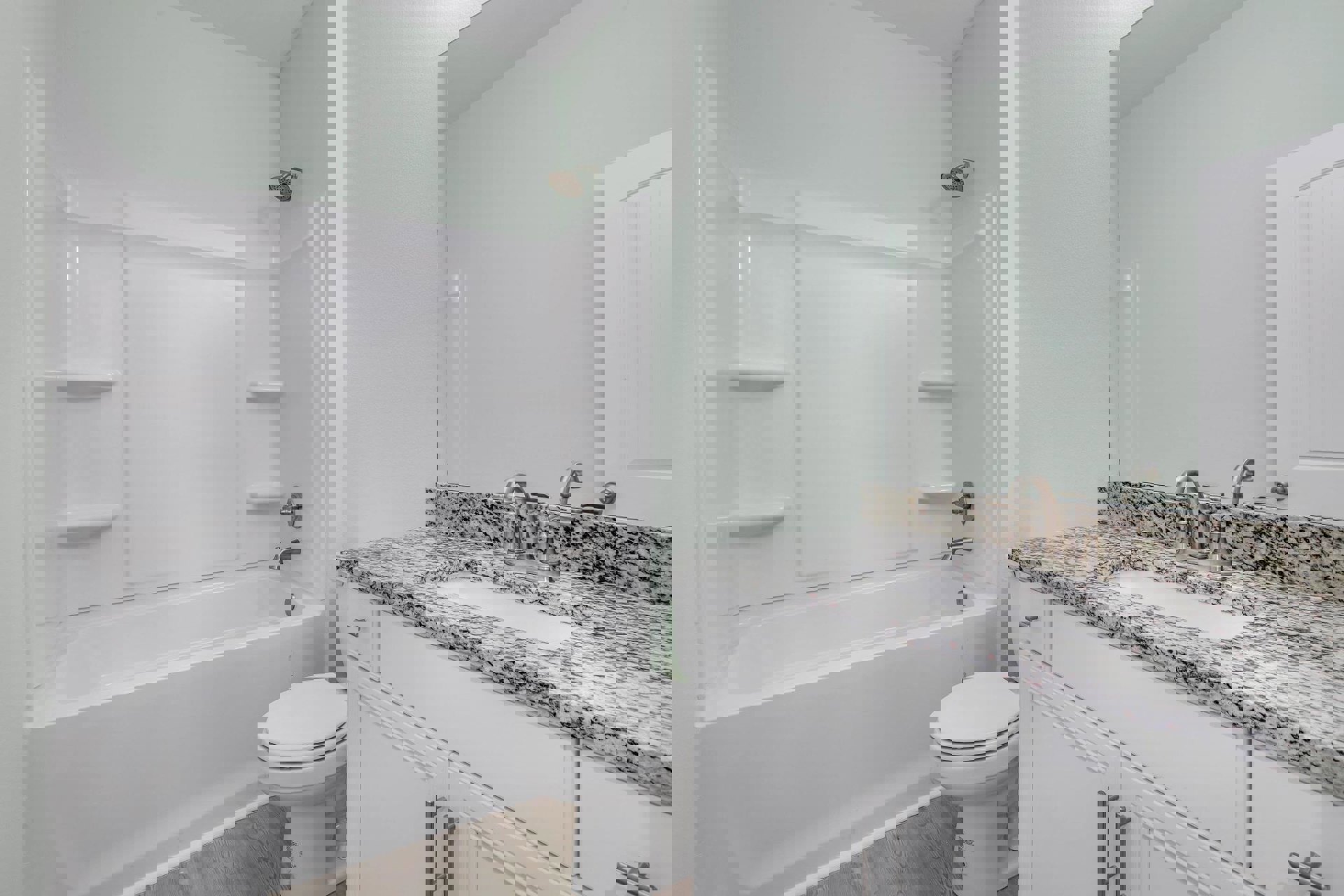 Bathroom featuring marble countertop and undermount sink, wall-mounted mirror, white toilet, tiled walls, chrome showerhead, and white bathtub.