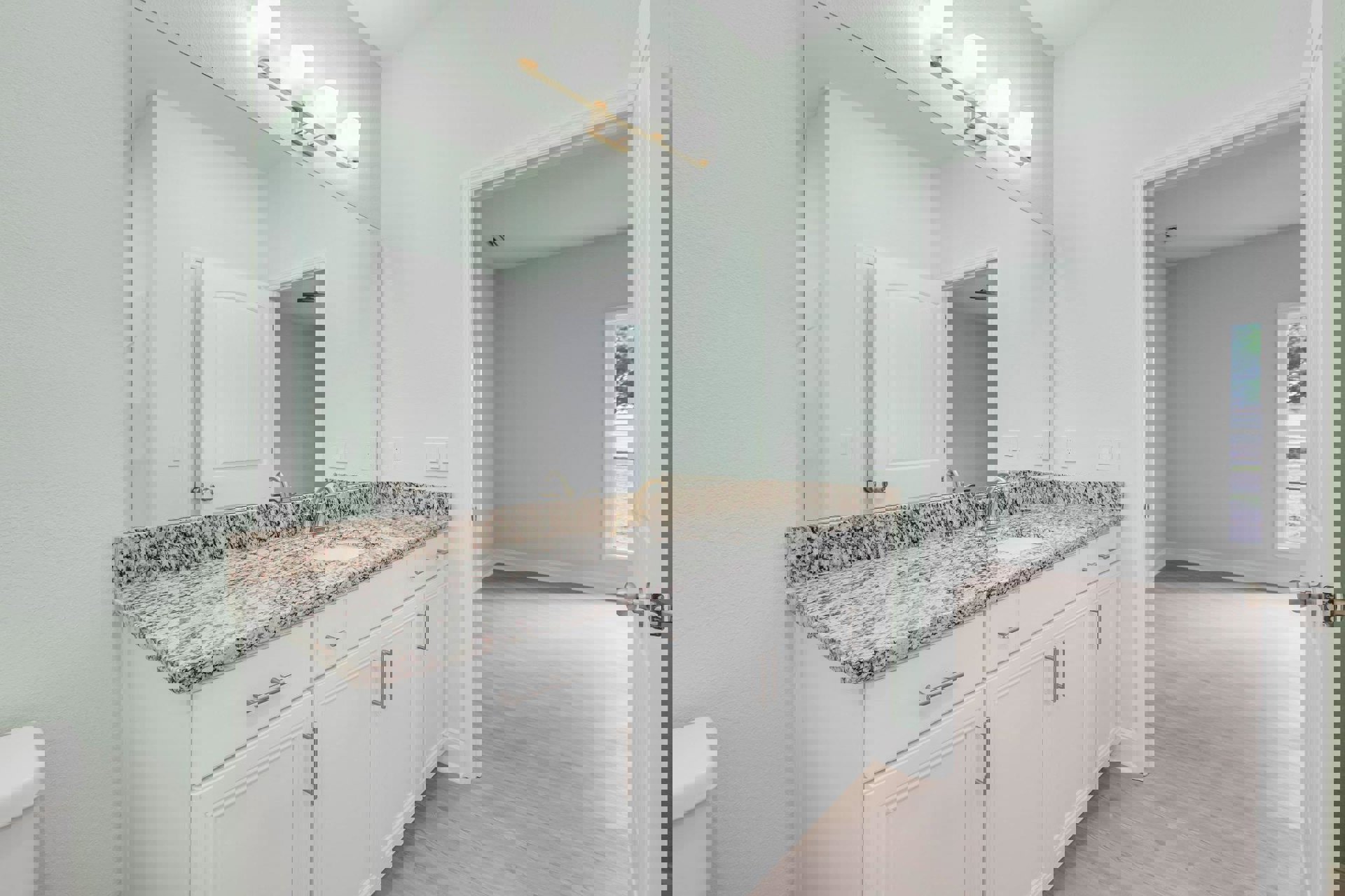 Bathroom featuring marble countertops and marble flooring, white sink set in a marble vanity, wall-mounted mirror above, four-light fixture, white toilet tank visible, cabinetry