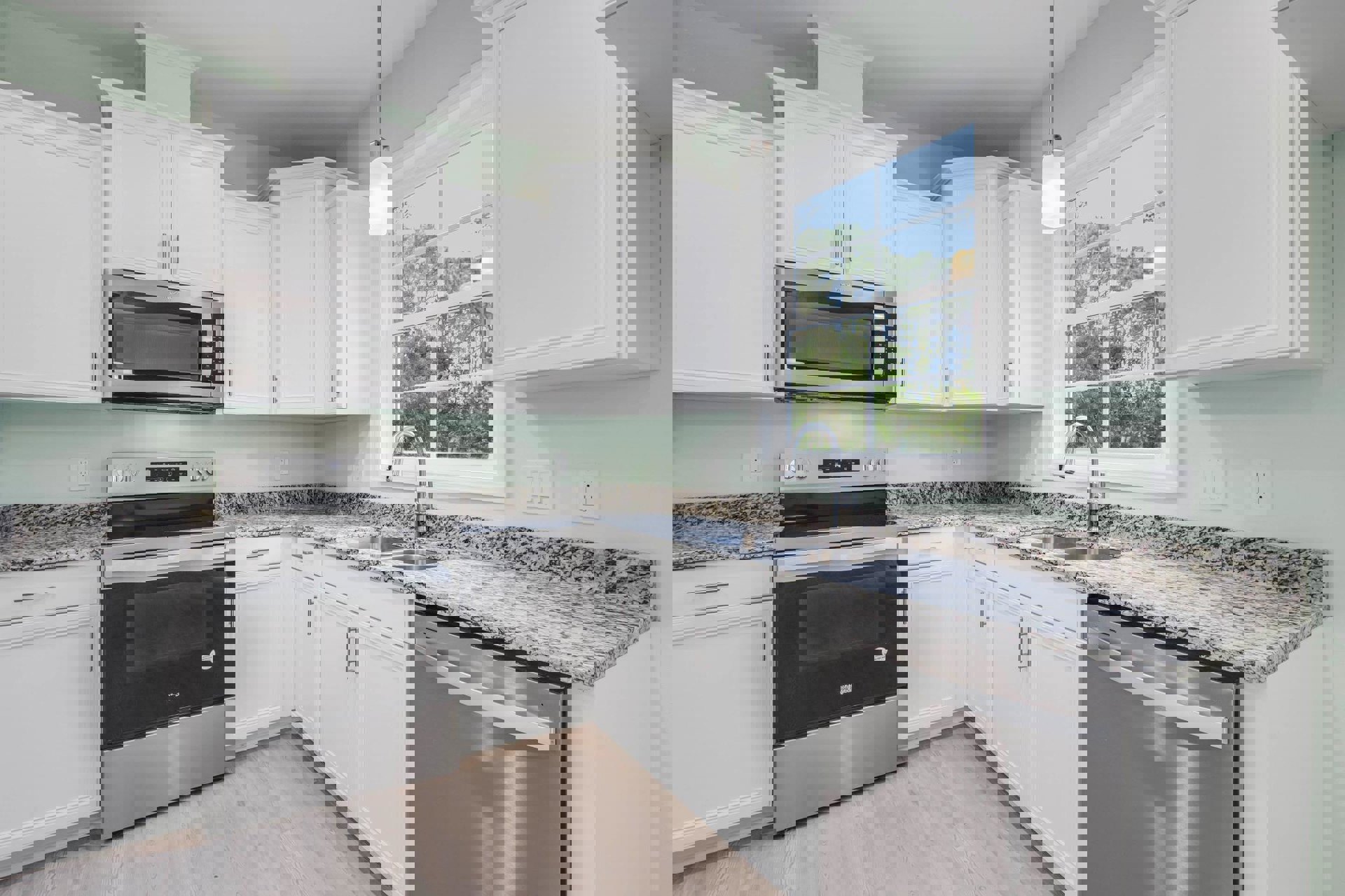 White kitchen cabinets, black appliances including open microwave and stove, stainless steel dishwasher beneath marble countertop, window overlooking trees, granite countertops