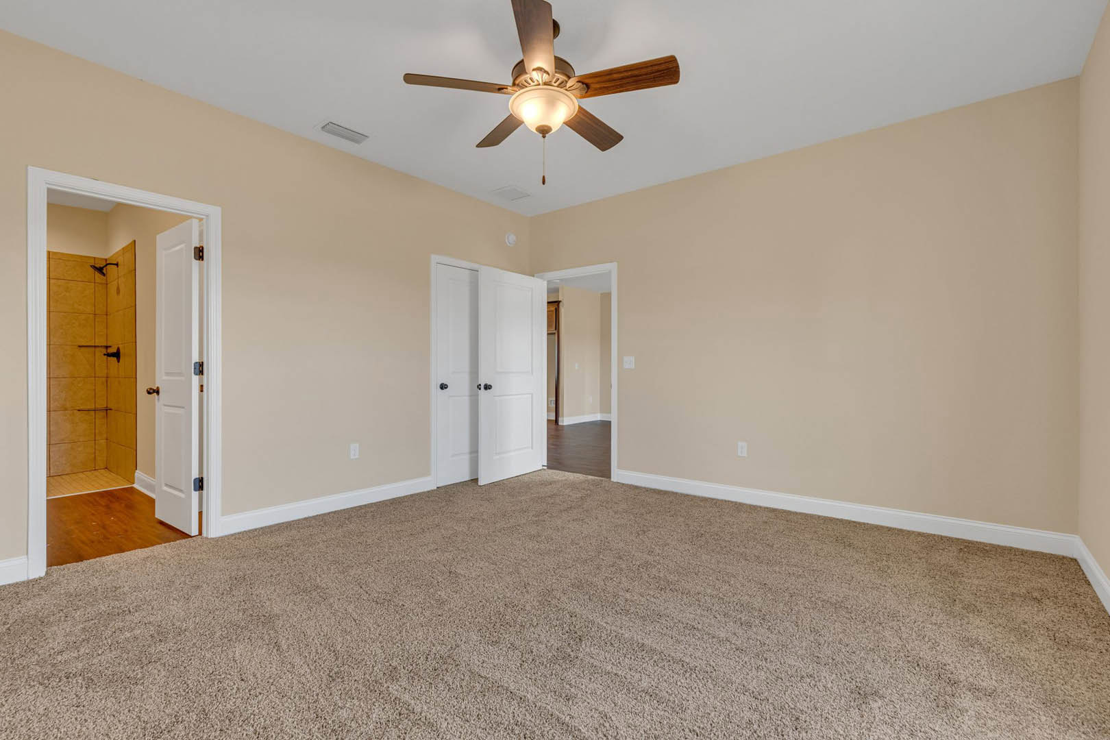Carpeted bedroom with white walls, ceiling fan with light fixture, open white door featuring black hardware