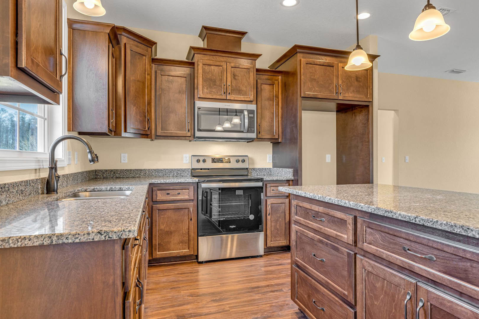 Granite countertops with wood cabinets, stainless steel oven with glass door, modern light fixtures above, chrome faucet, marble-topped drawers
