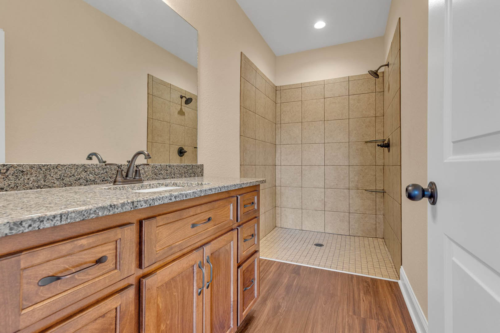 Modern bathroom featuring tiled shower with glass door, granite countertop vanity with undermount sink, chrome faucet, and white cabinetry
