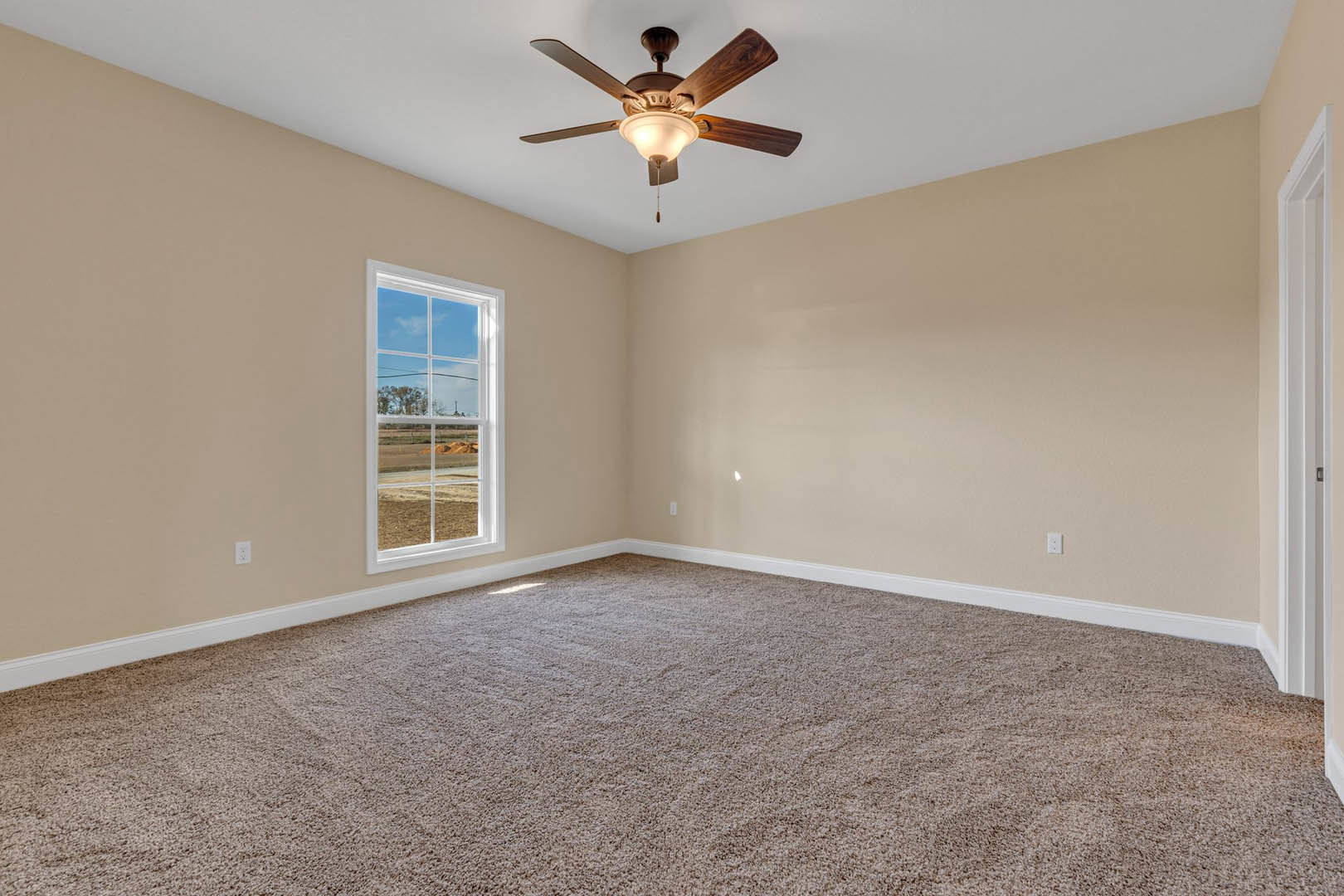Bedroom with beige carpet, white walls, ceiling fan with light fixture, large window overlooking grassy field, simple baseboard molding