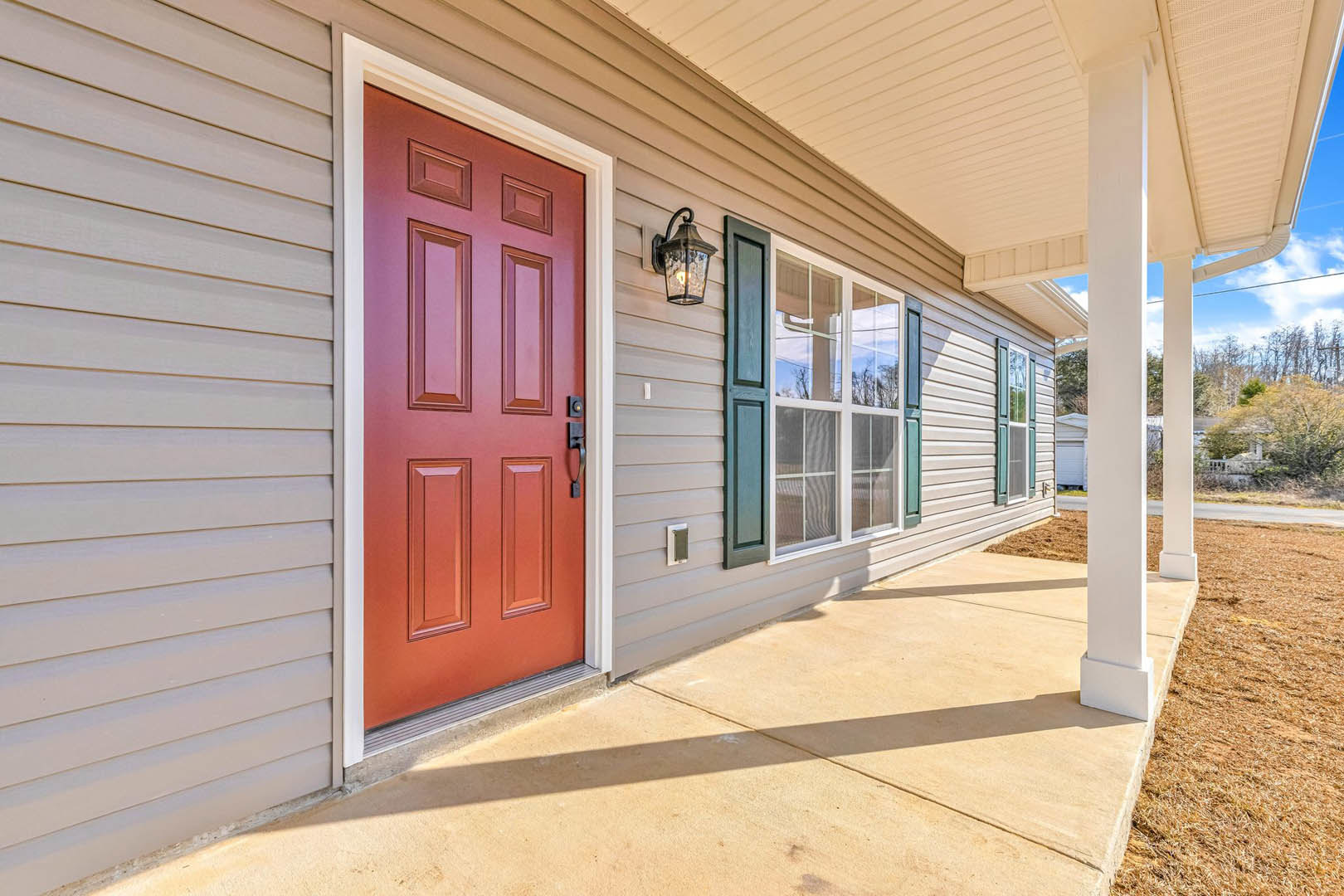 White siding house exterior with a prominent red front door, blue shuttered window, and sunlight casting shadows across entryway and facade