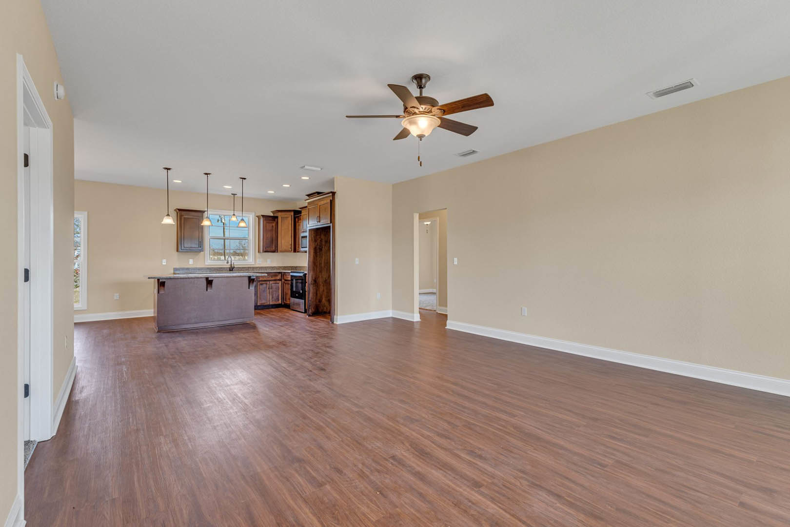 Spacious open floor plan featuring hardwood flooring, wood paneled wall, ceiling fan with light, and neutral-toned surfaces.