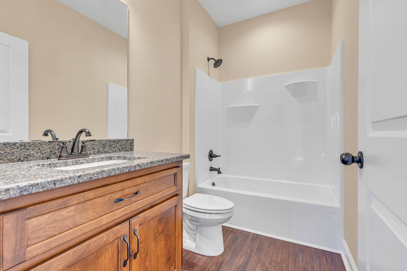 Bathroom with white bathtub and closed-lid toilet, marble countertop vanity, white walls, wooden door frame, and chrome door knob