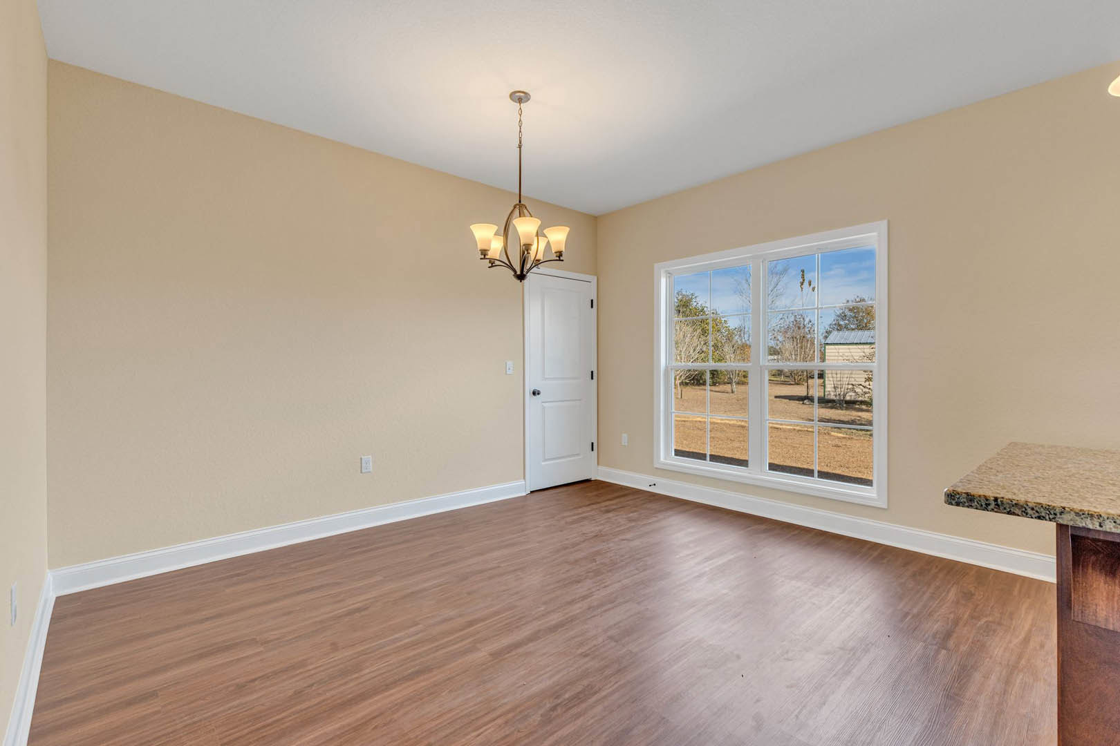 White paneled door with black handles, large window overlooking green yard, hardwood flooring, marbled table, modern chandelier, neutral walls