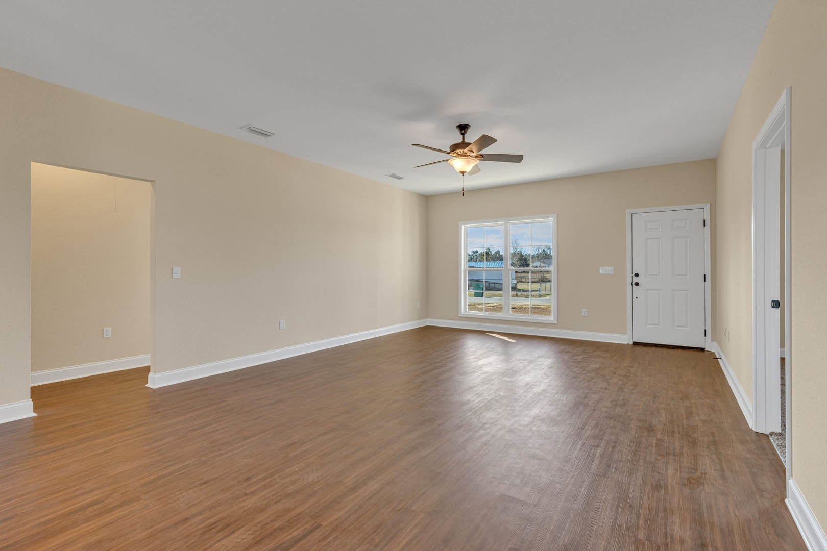 Ceiling fan with light on white ceiling, hardwood floor, white door with black knobs, window overlooking farm, neutral walls