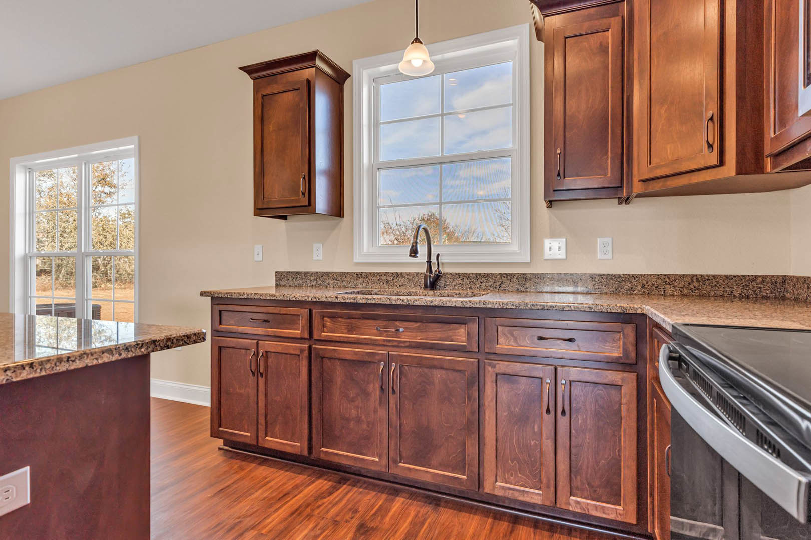 Marble kitchen island with built-in sink and chrome faucet, white cabinetry, stainless steel stove, large window overlooking trees, under-cabinet lighting