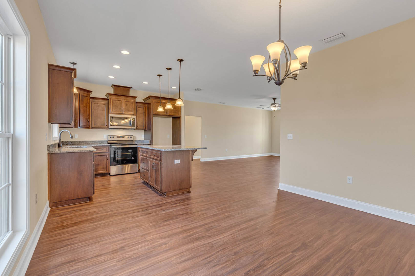 Open kitchen and dining area with hardwood floors, white cabinetry, marble-topped island with drawers, stainless steel oven, and modern chandelier above the dining table.
