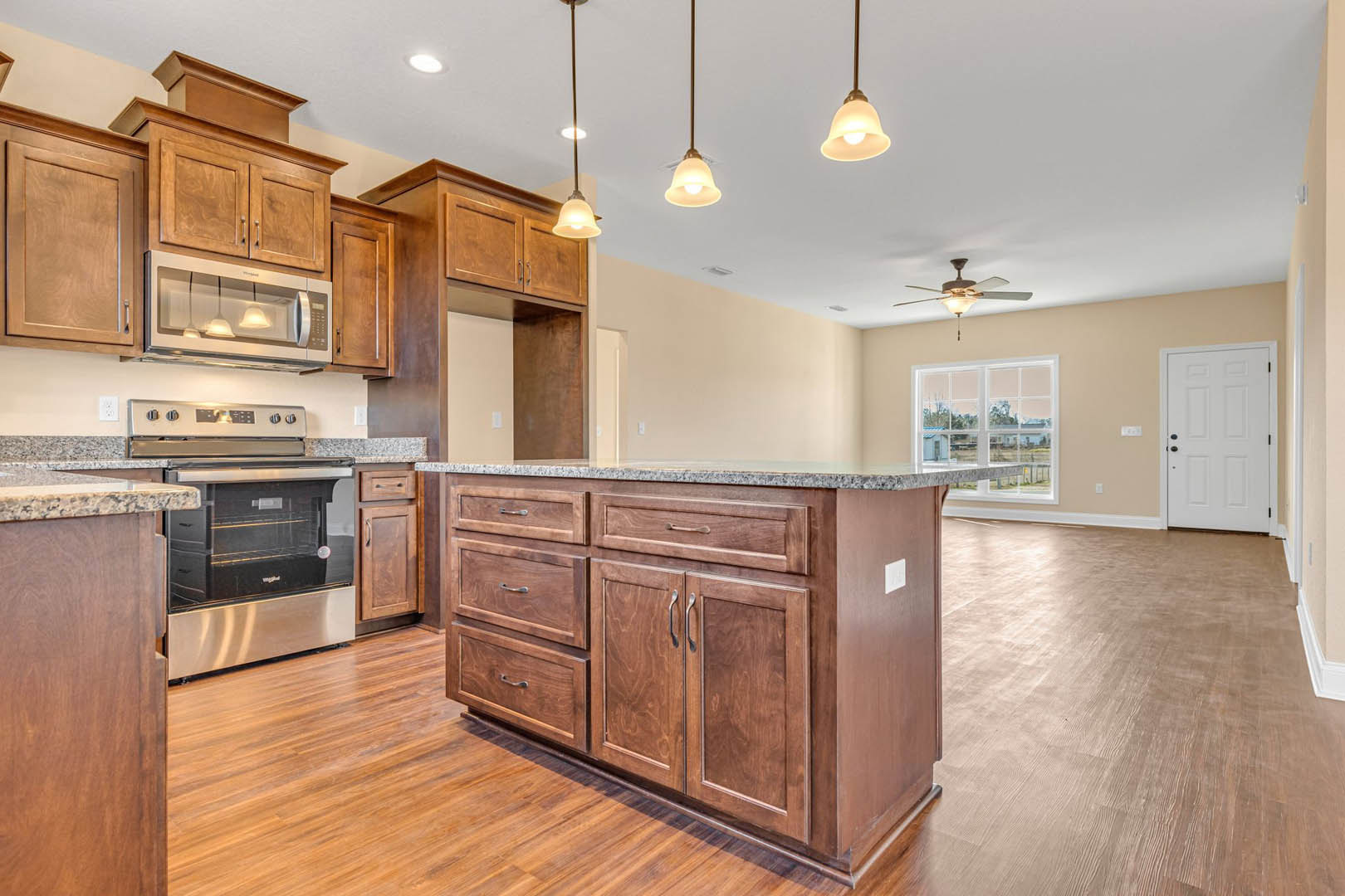 Spacious kitchen featuring a large central island with stone countertop, wood flooring, white cabinetry with black knobs, built-in microwave and oven, ceiling pendant lights, and a