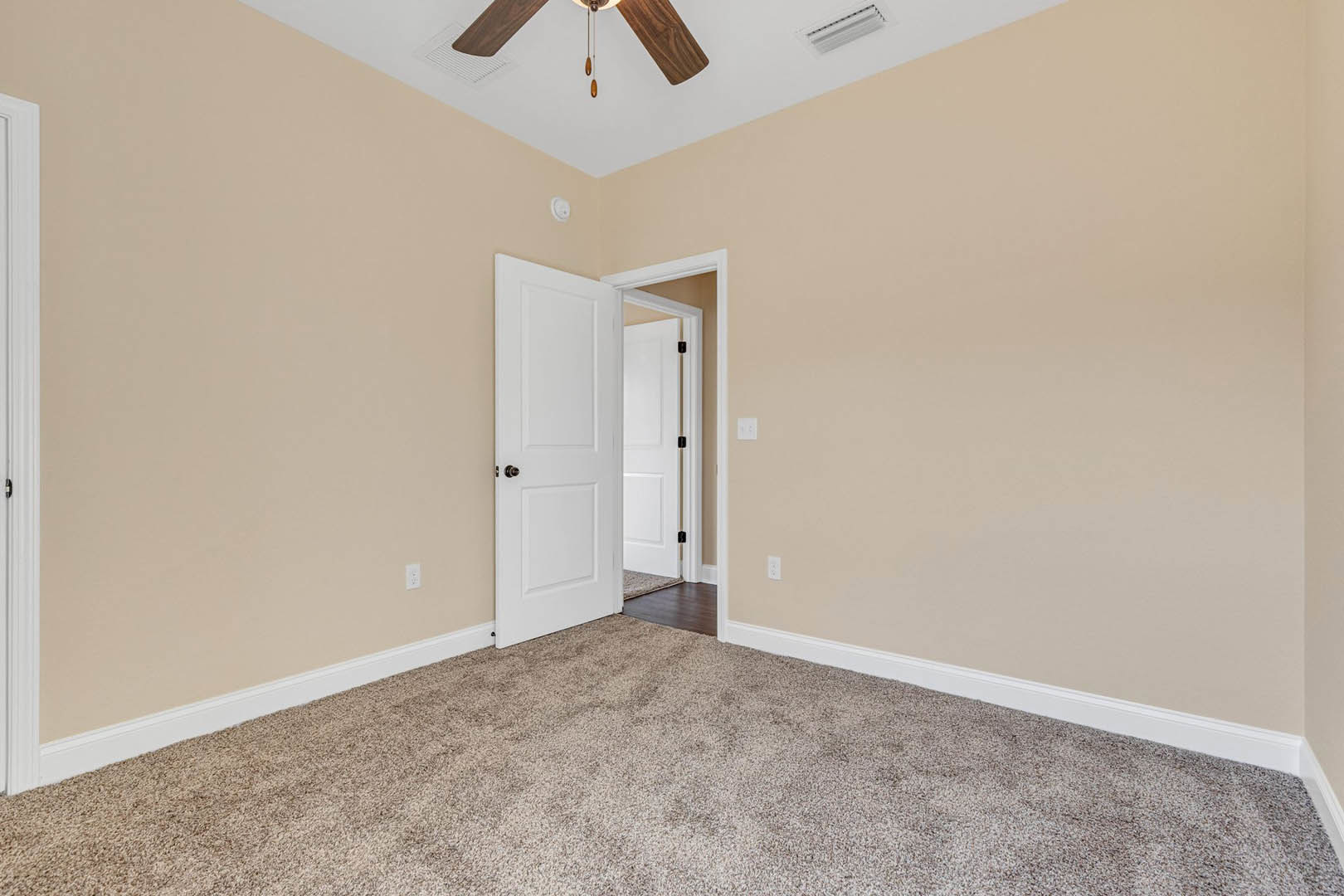 Neutral-toned room with carpet flooring, white paneled door featuring a black handle, ceiling fan with wooden blades, and simple wall molding.