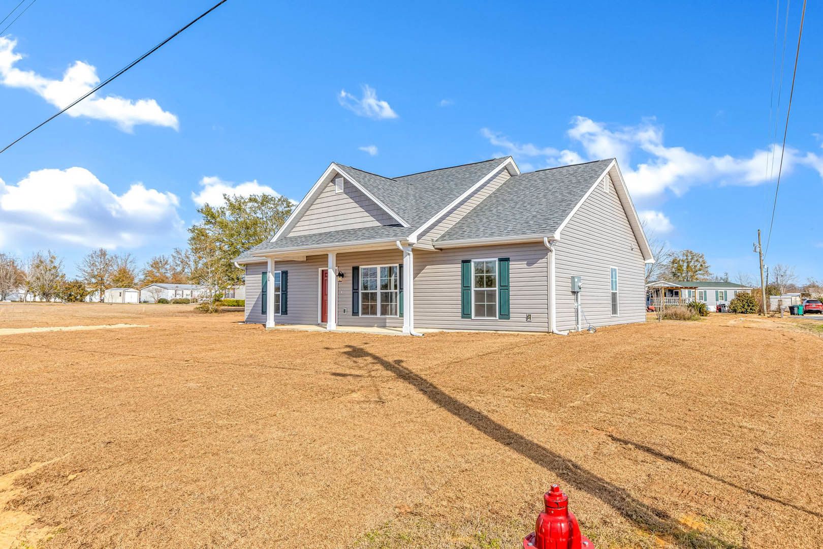 Red fire hydrant on green lawn in front of a white house with green shutters, large windows, and shaded facade