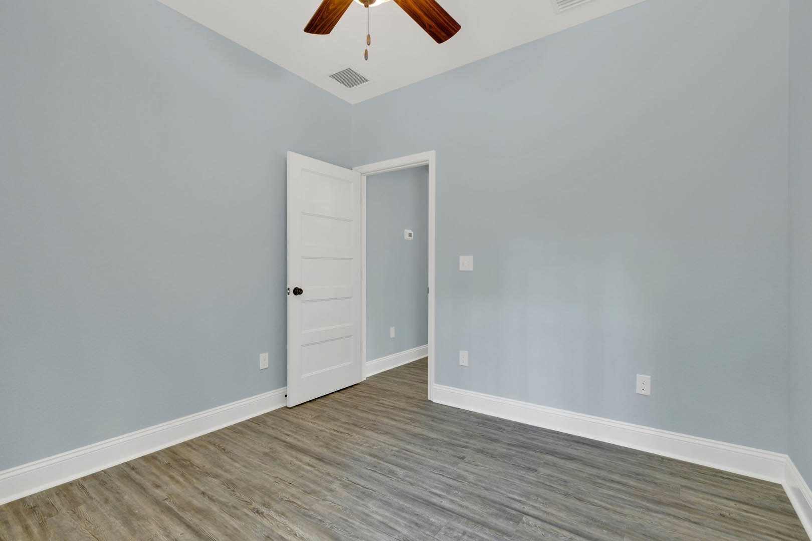 Wood flooring with white baseboards, white walls, white door featuring a black knob, and a ceiling fan with dark blades and light fixture