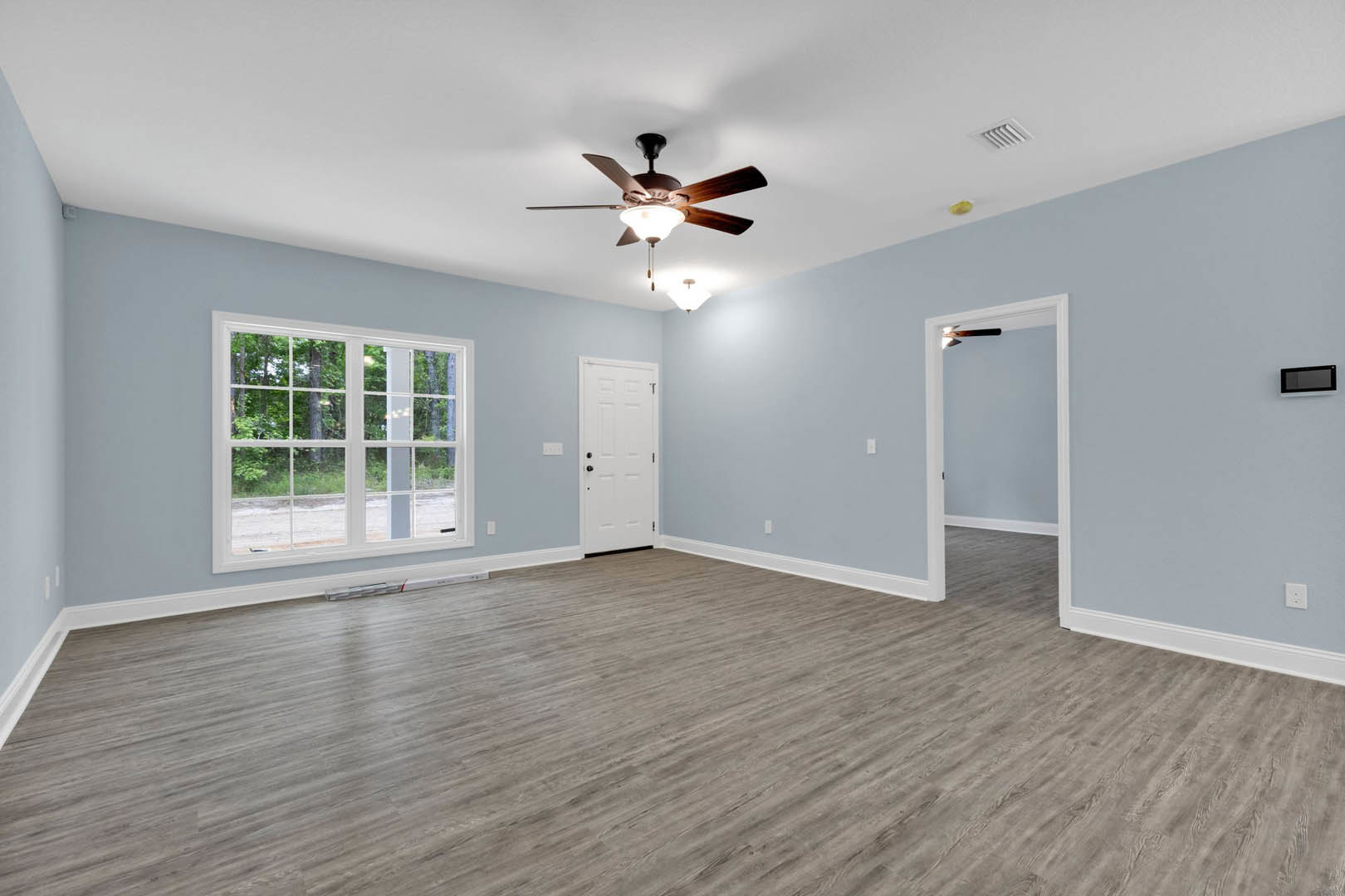 Ceiling fan with light fixture, wood flooring, white door with black knobs, window overlooking trees, plaster walls, ceiling vent
