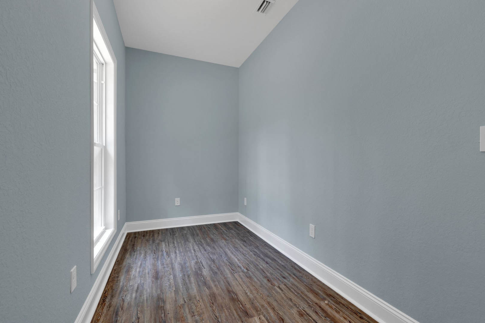 Wood flooring with white baseboards, white walls, and a rectangular window letting in natural light