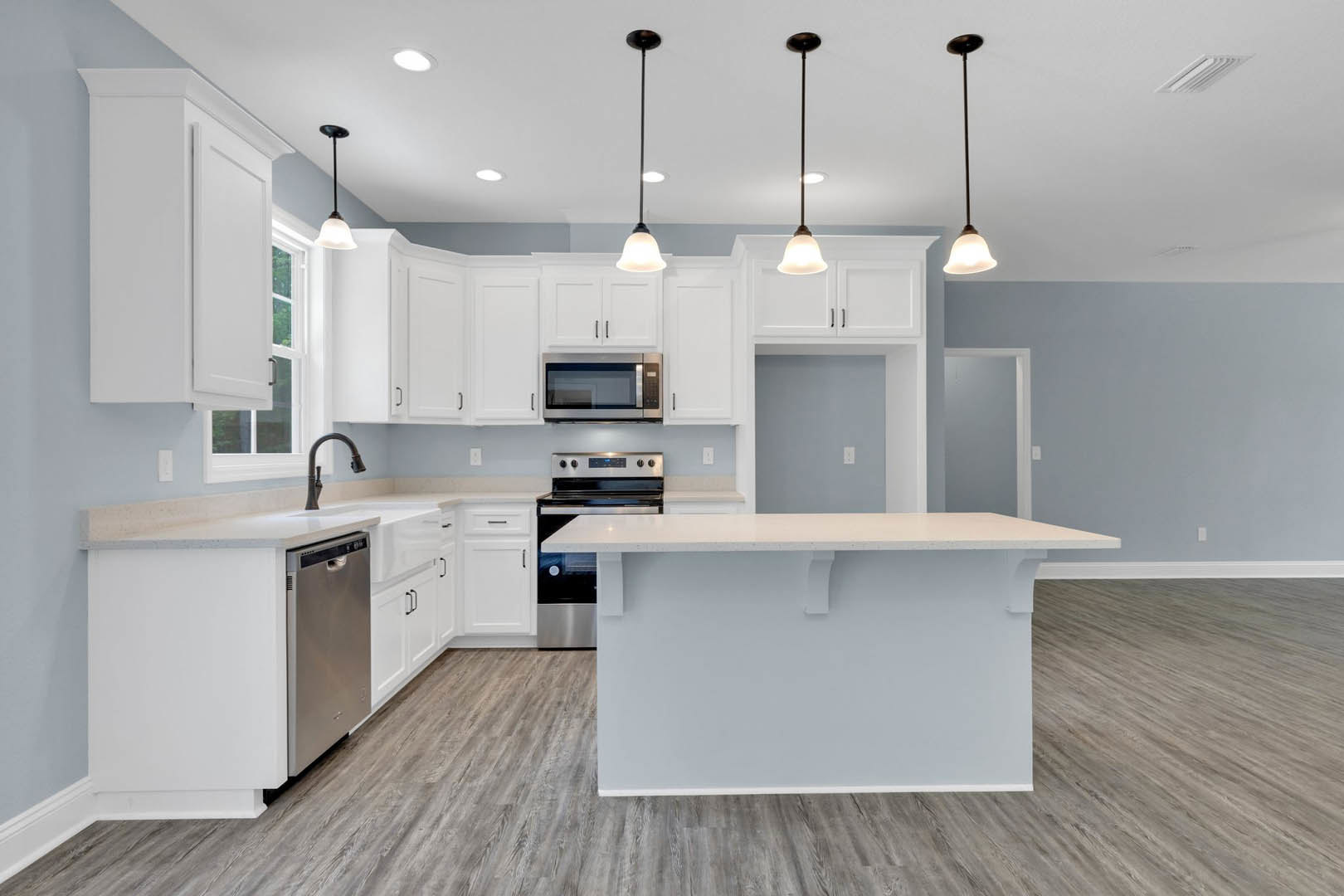 White kitchen with shaker cabinets, large white island, quartz countertops, built-in microwave, pendant lighting, and open shelving.