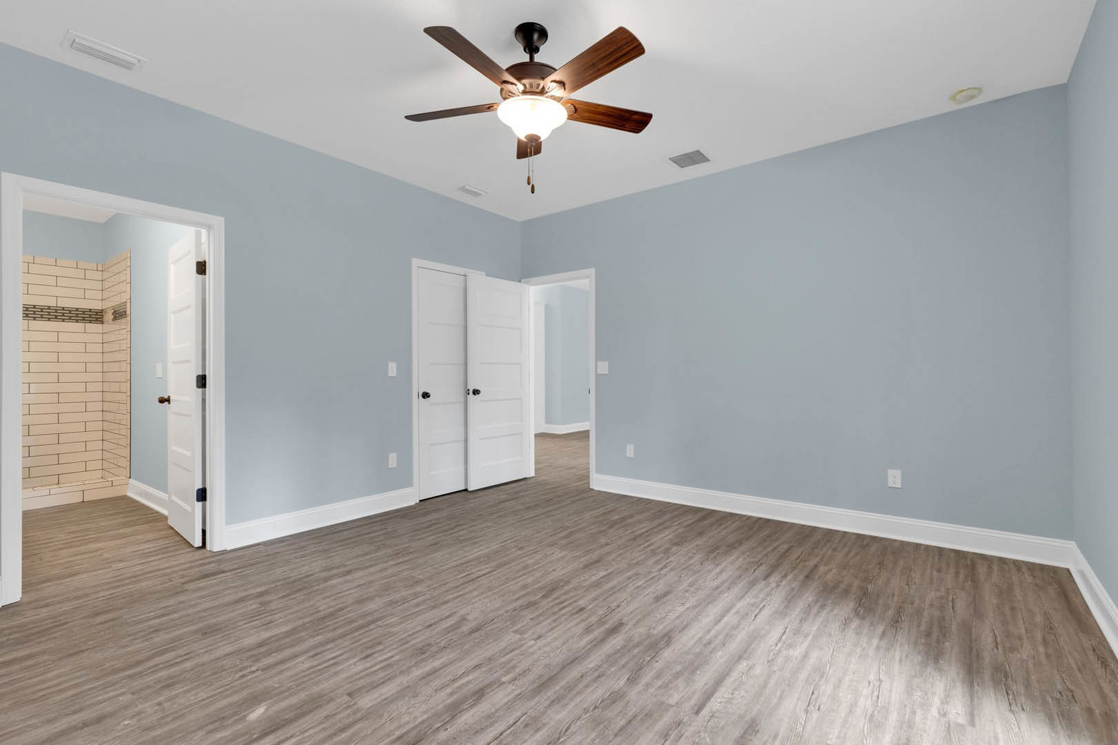 Wood flooring with white doors, ceiling fan with light fixture, white tile shower wall, black door knobs