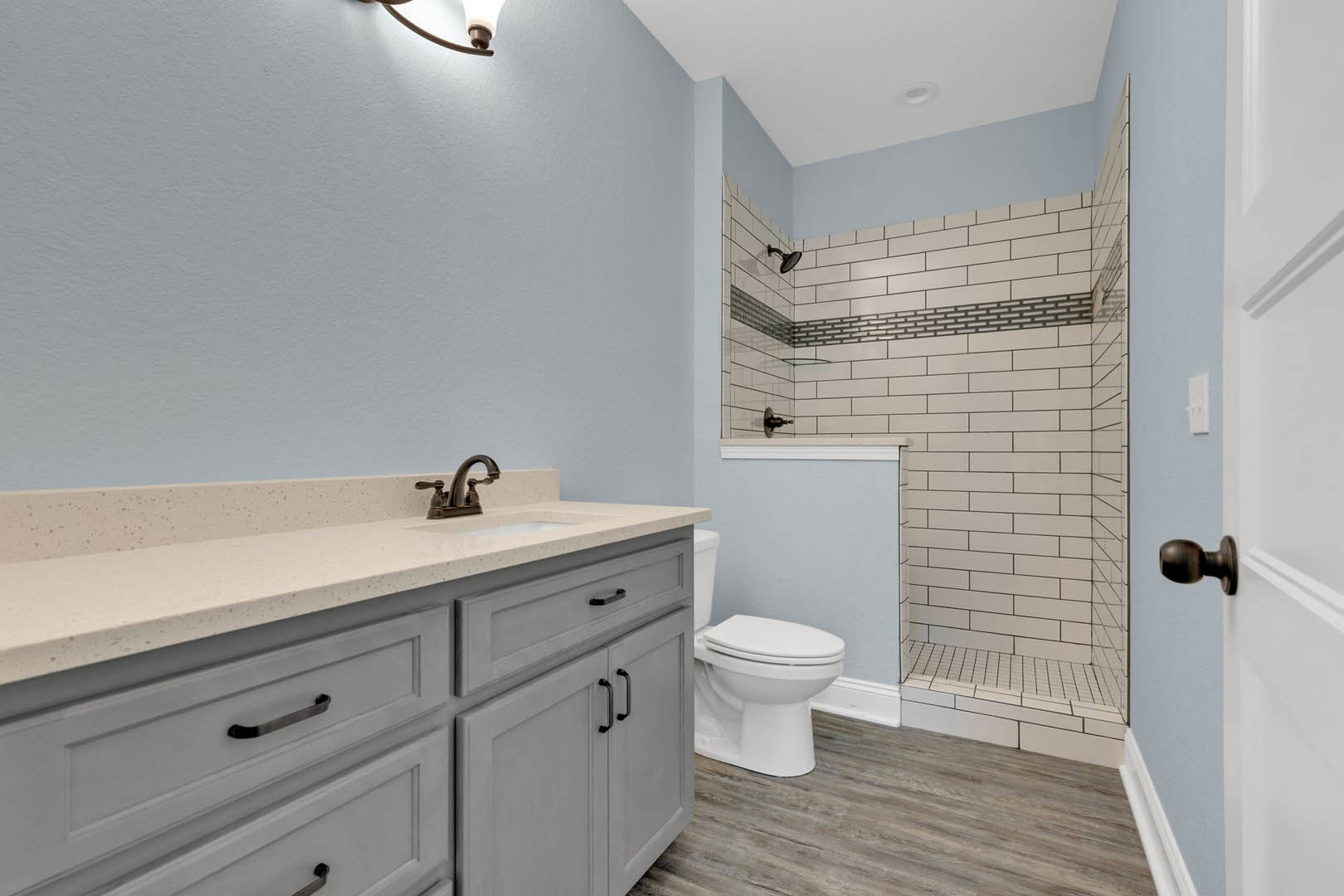 Bathroom with wood flooring, white toilet, white sink with chrome faucet, glass-enclosed shower, and light-colored tile walls