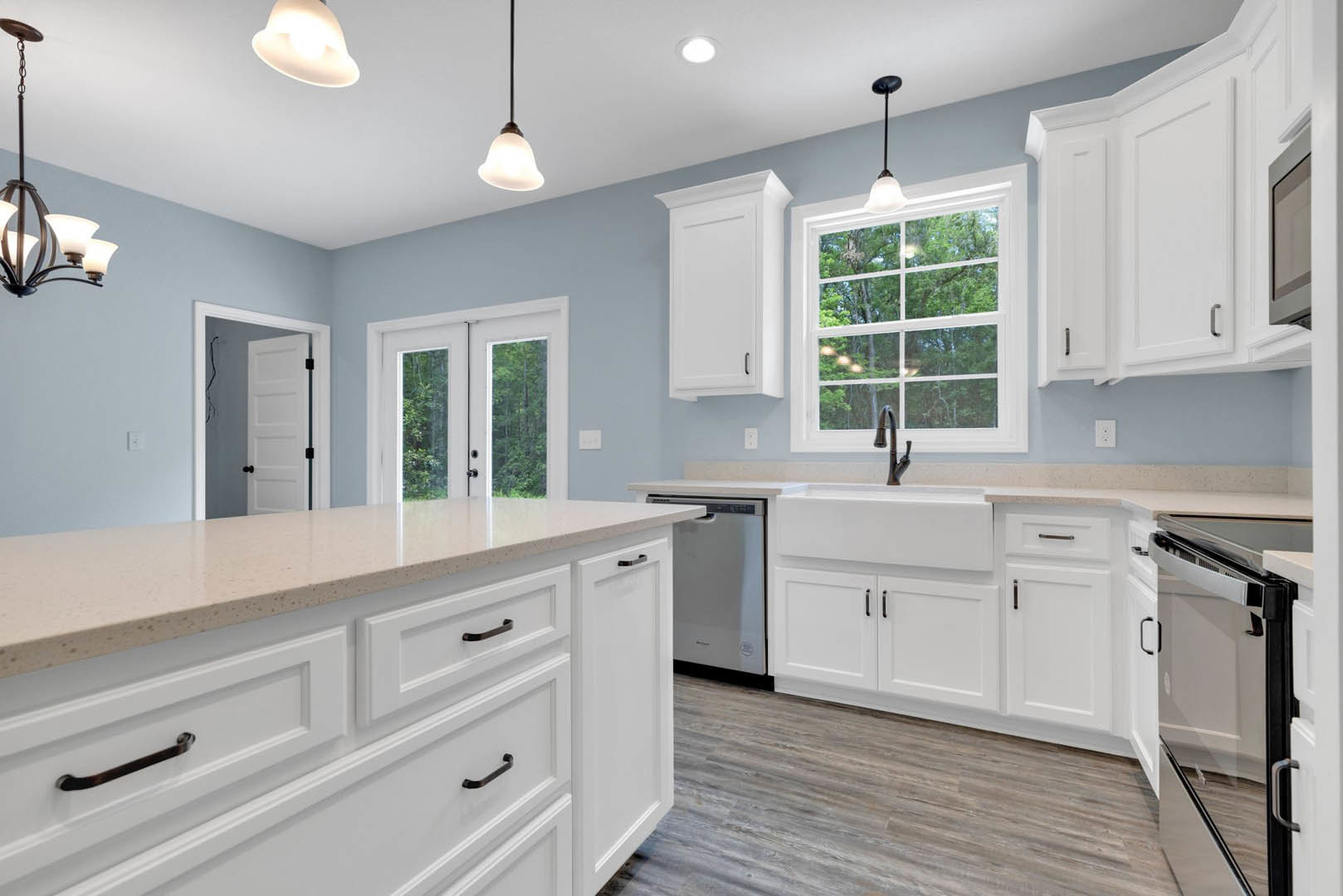 White kitchen with shaker cabinets, black hardware, undermount sink, quartz countertop, large window overlooking trees, and modern pendant chandelier