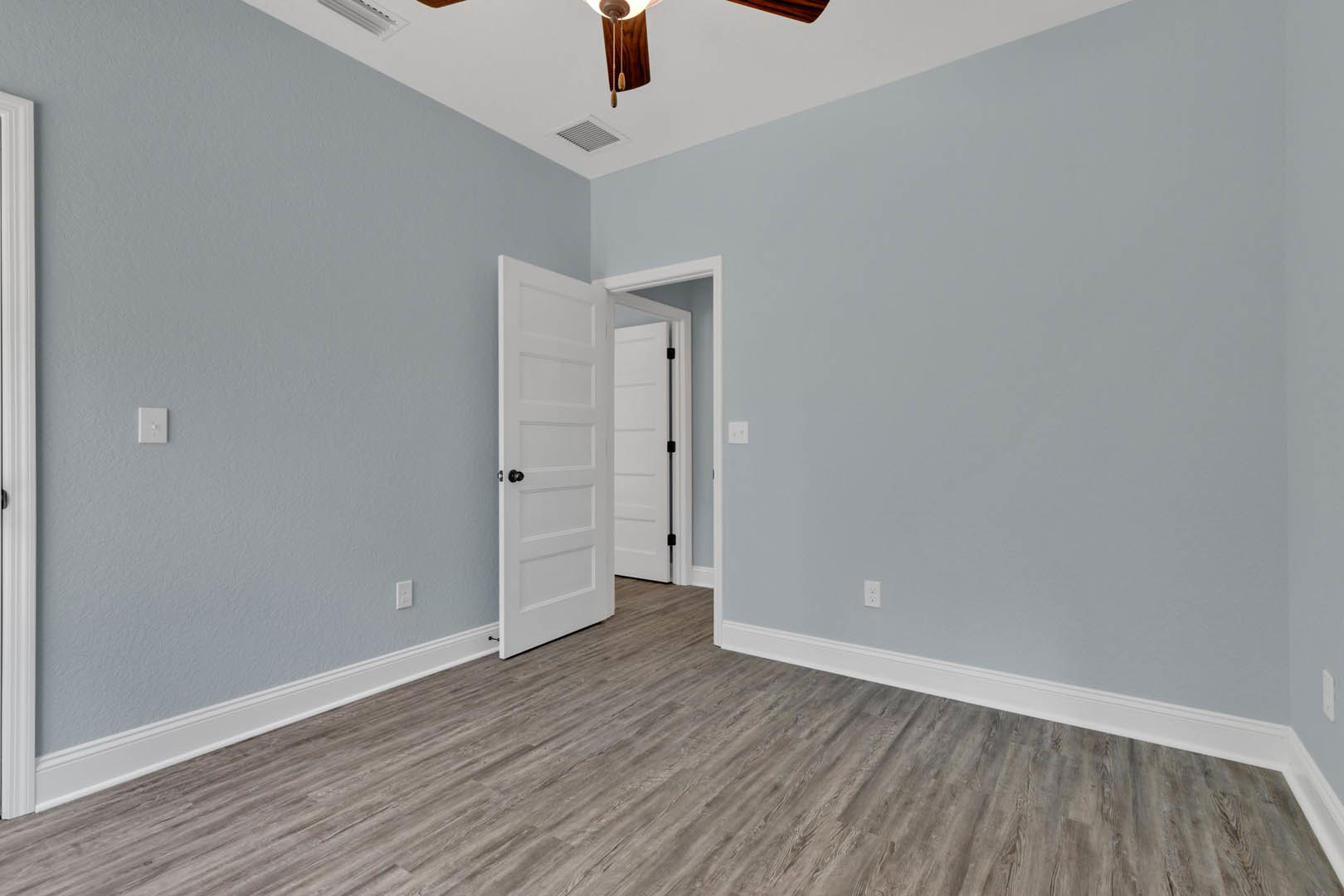 Ceiling fan mounted on white ceiling, white door with black handle, wood laminate flooring with white trim, white walls, white light switch, white door frame