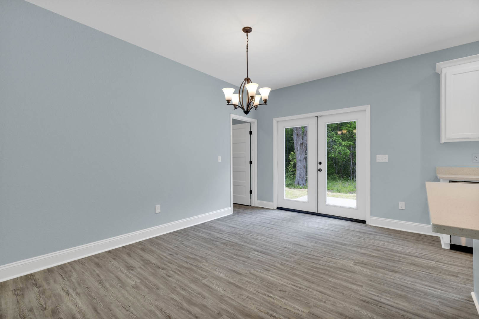 White double doors with glass panes, hardwood flooring, ornate chandelier, large window revealing trees outside, plaster walls